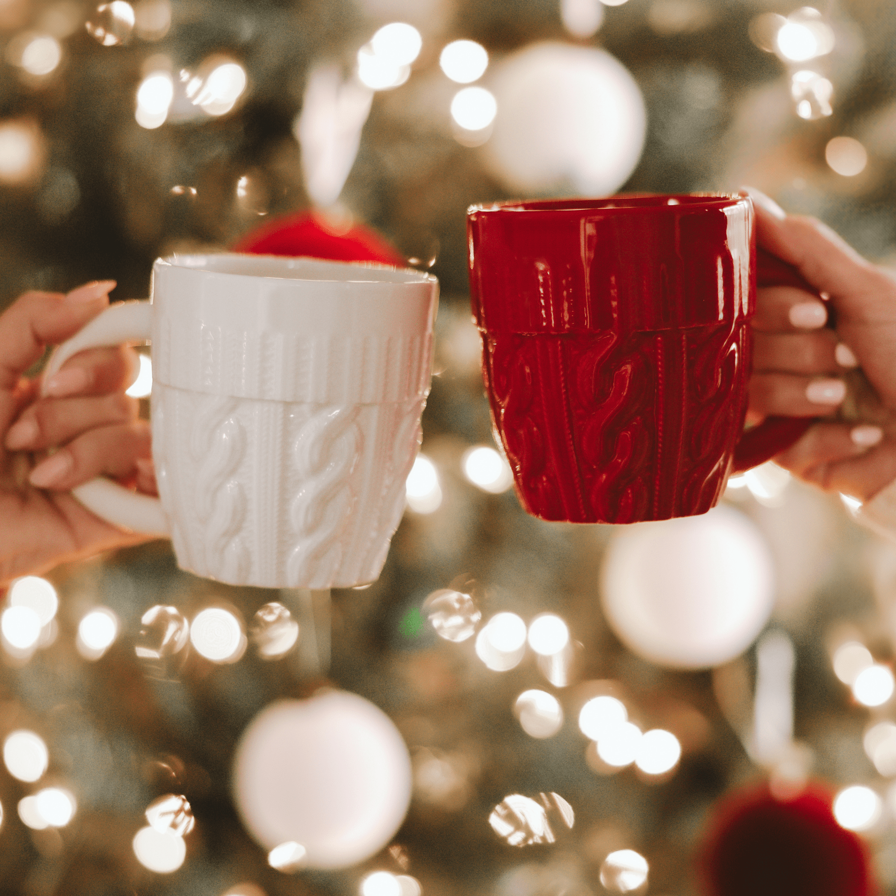 Two ceramic mugs held up against festive Christmas tree lights, one cream-colored and one deep red, both featuring a textured sweater knit pattern design.