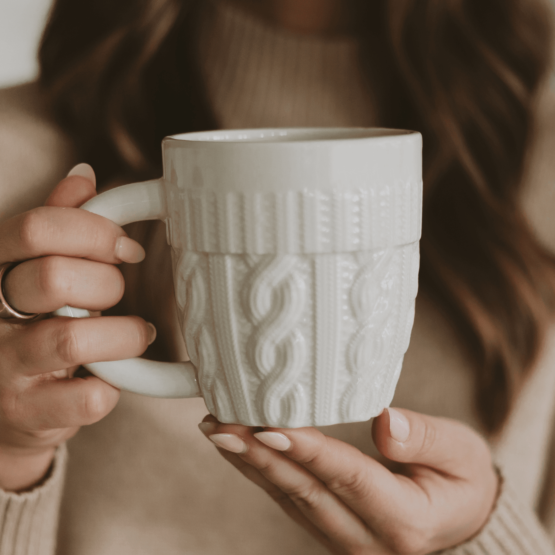 Cream ceramic mug with cable knit sweater texture design, held in hands