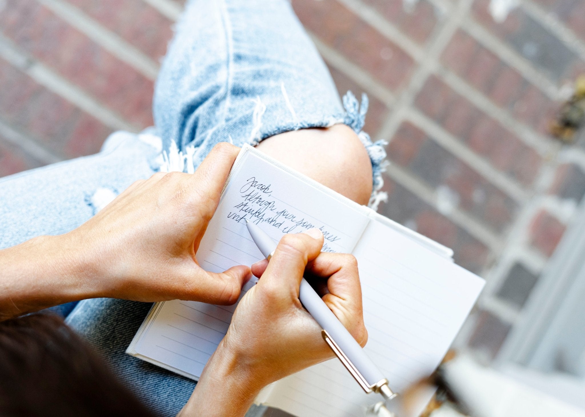 Hand holding open white vow book with handwritten text, displayed against brick background