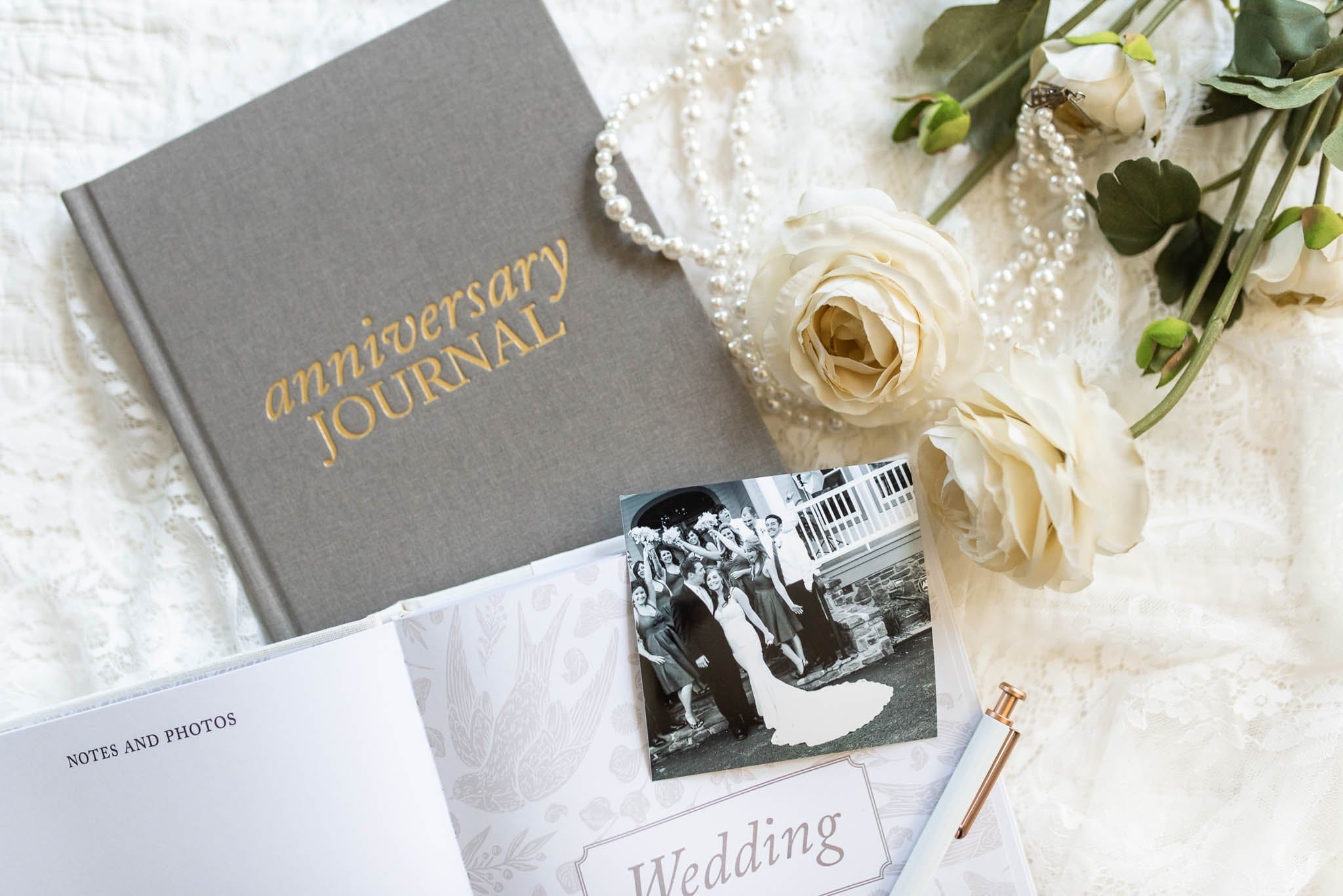 Gray hardcover anniversary journal with gold foil lettering, displayed with wedding photos and cream roses on white fabric