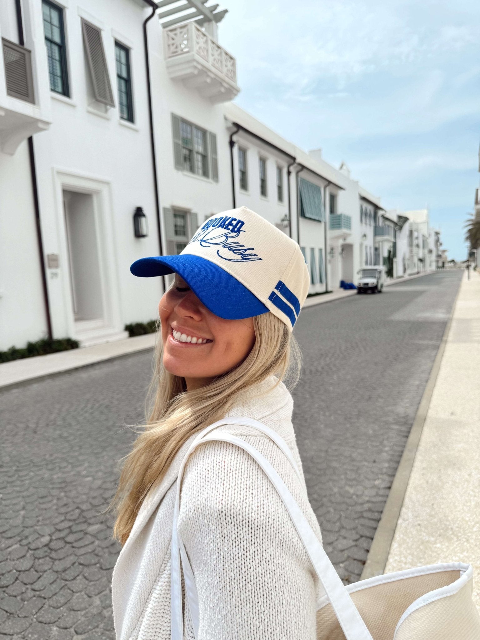 Woman wearing royal blue and white vintage trucker hat with "Booked and Busy" text and graphic design