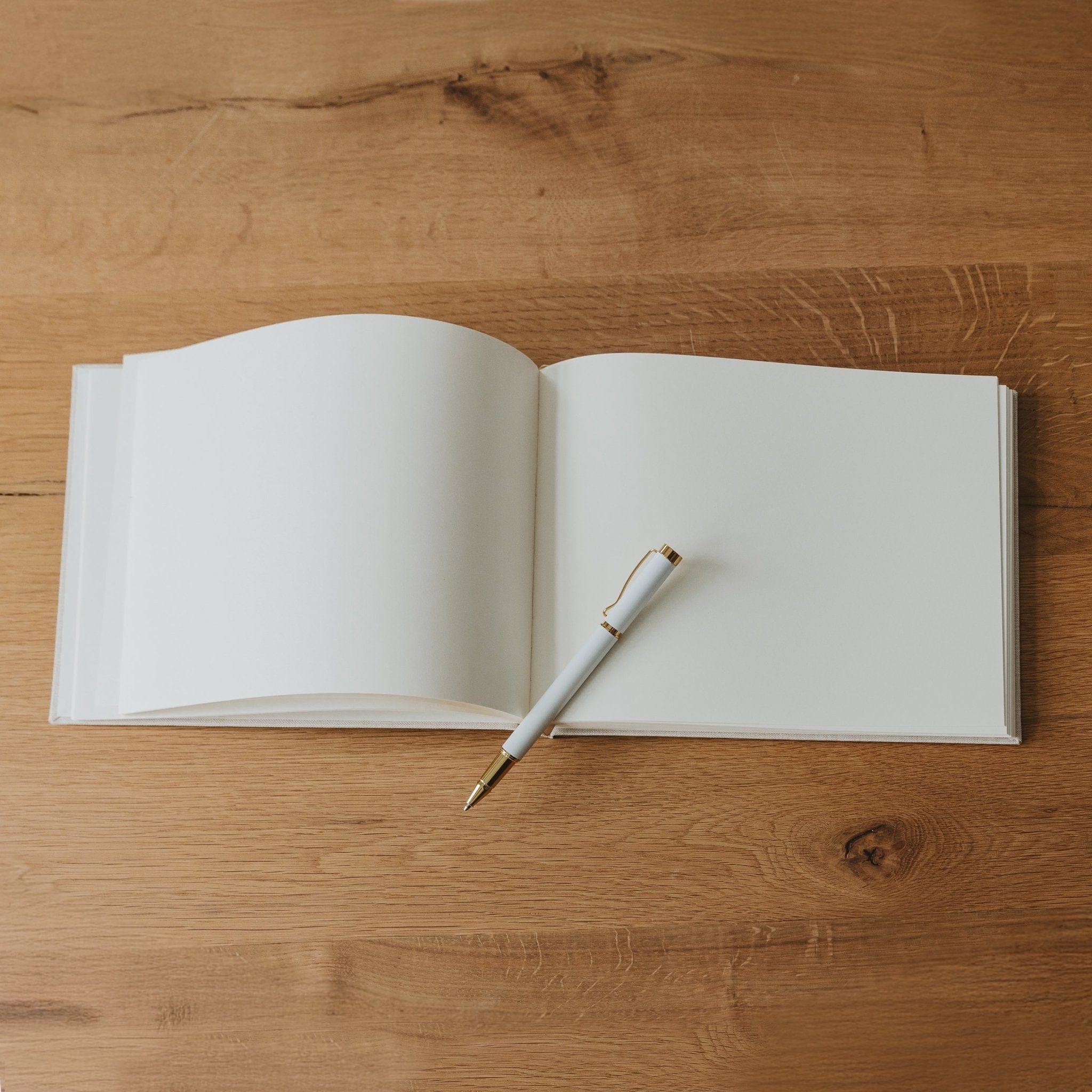 Open tan guestbook with blank white pages and pen on wooden surface