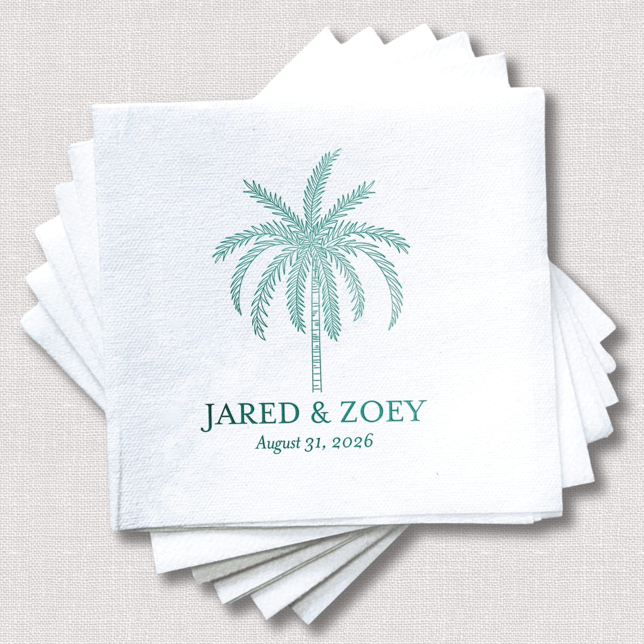 Stack of white linen napkins with teal foil-stamped palm tree design and personalized names "Jared & Zoey" with wedding date August 31, 2026.