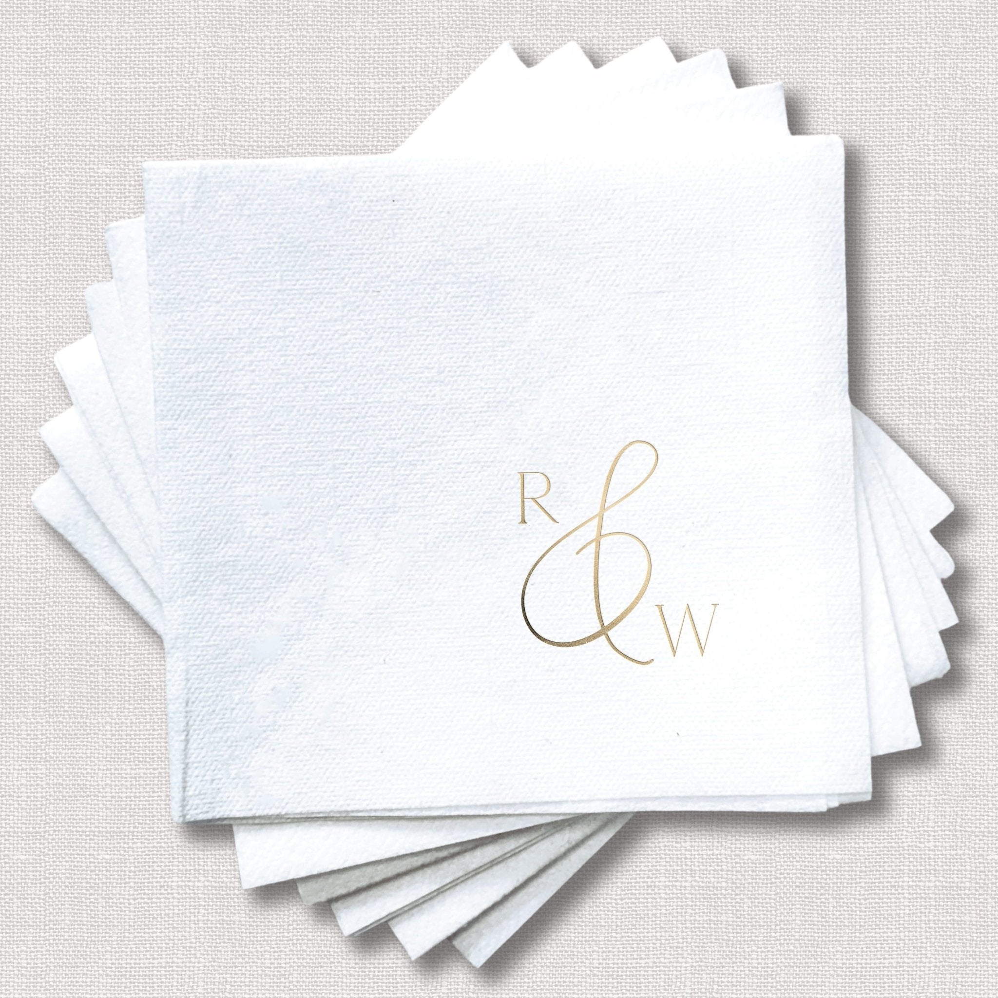 Stack of white linen napkins with gold foil monogram initials R and W in elegant script design.