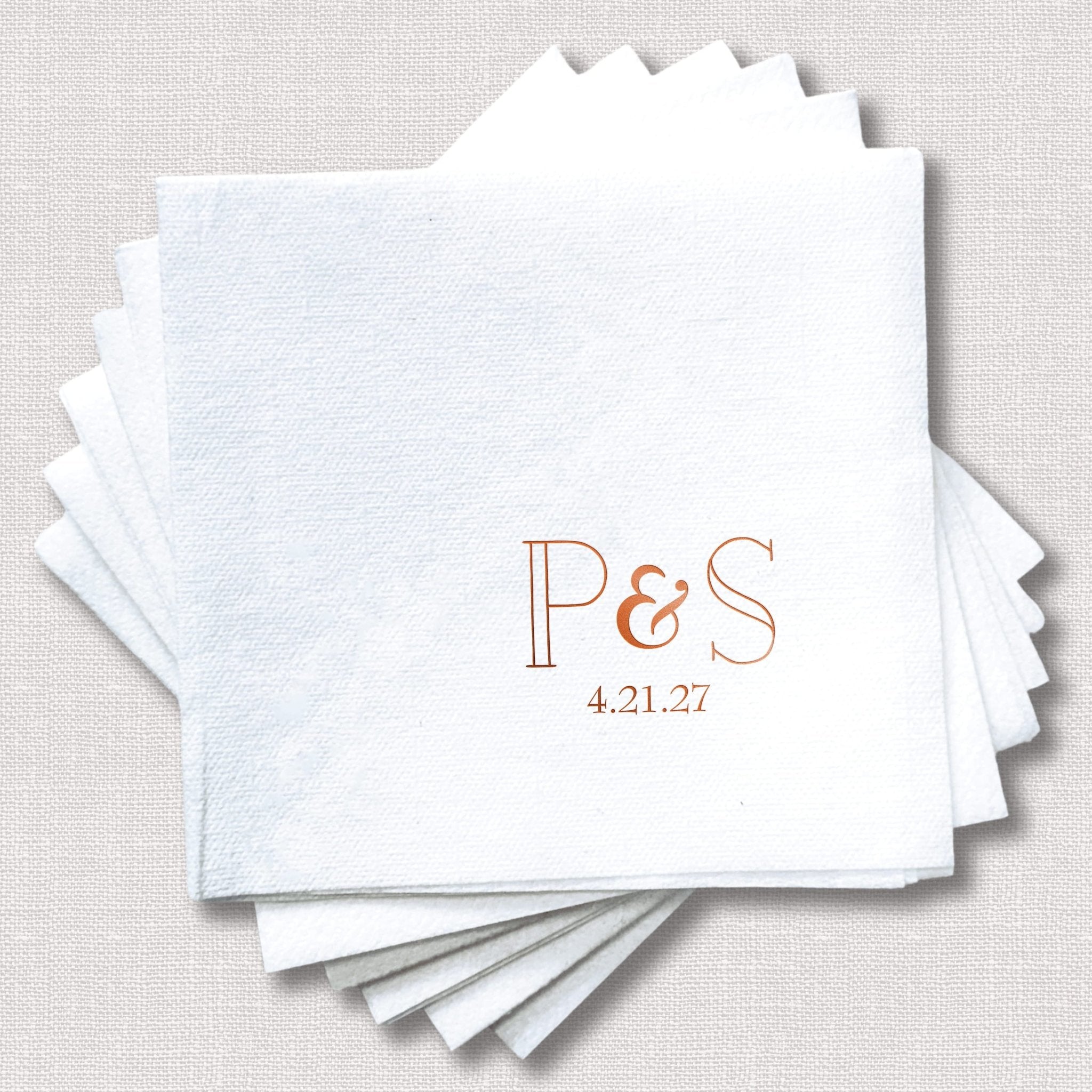 Stack of white linen napkins with rose gold foil stamped initials P&S and date 4.21.27