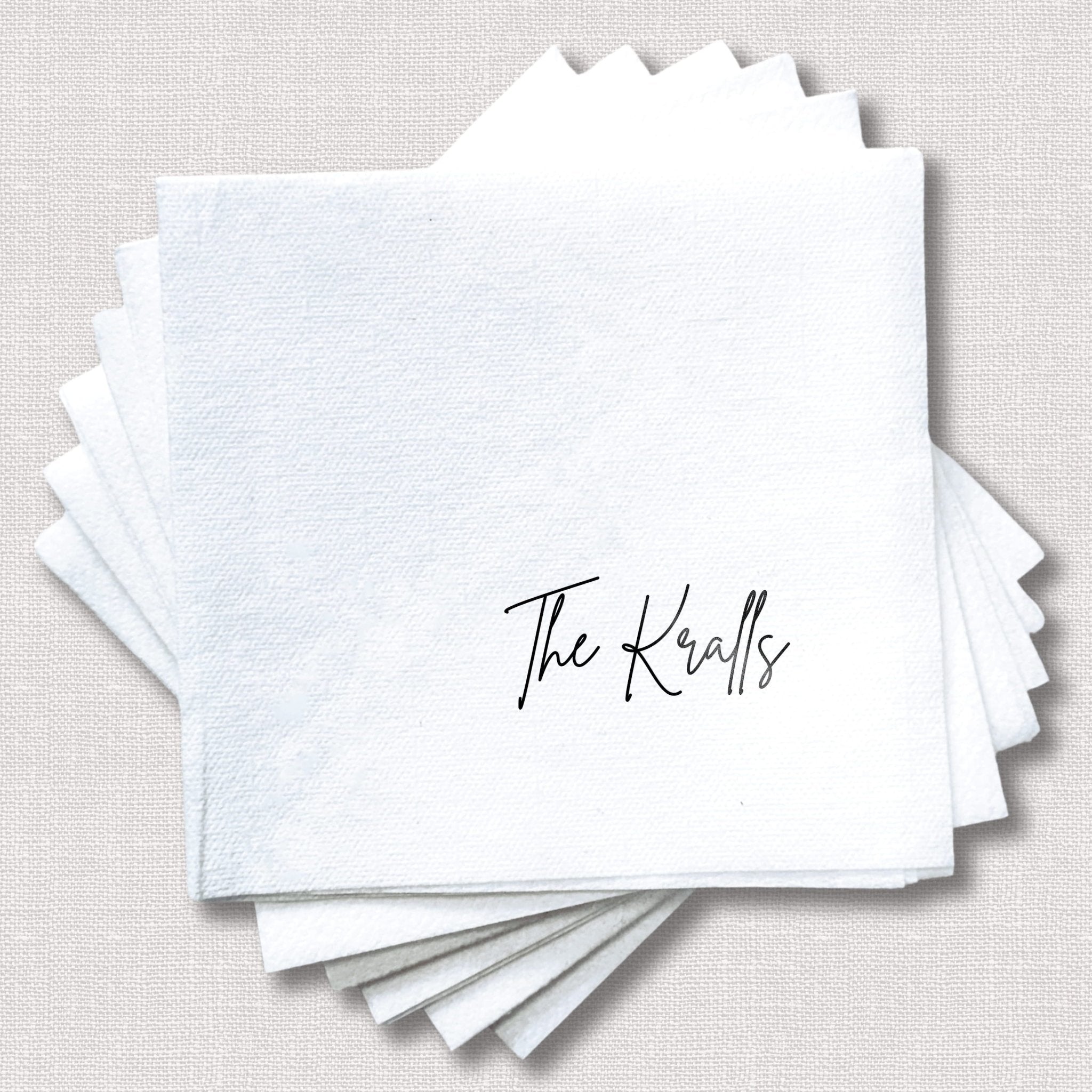 Stack of white linen napkins with scalloped edges and "The Kralls" printed in script in the corner