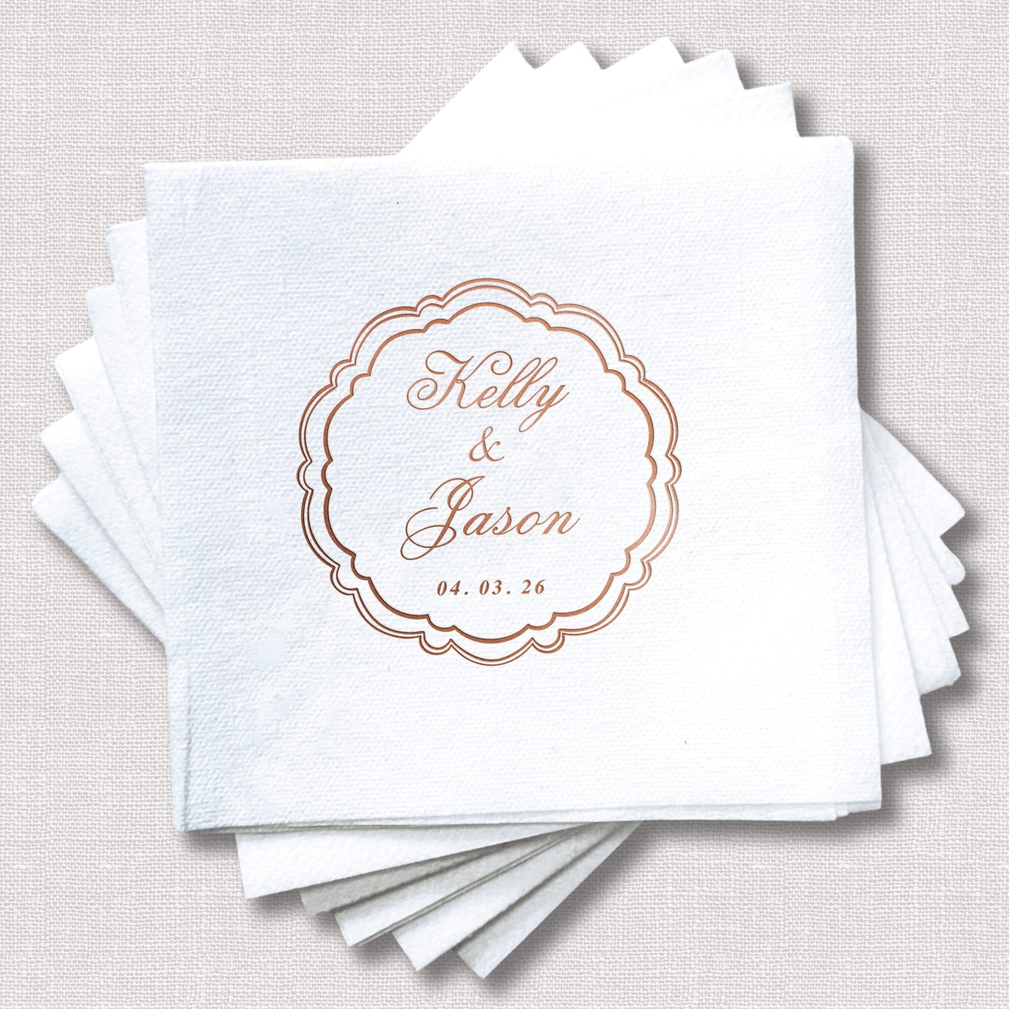 Stack of white cocktail napkins with rose gold scalloped frame design featuring personalized names Kelly and Jaxon with wedding date 04.03.26