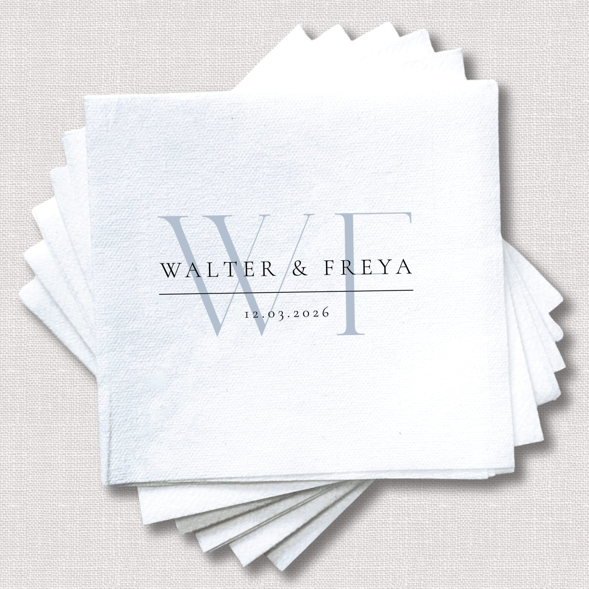Stack of white cocktail napkins with monogram initials WF, names Walter and Freya, and wedding date 15.03.2026 in blue text.