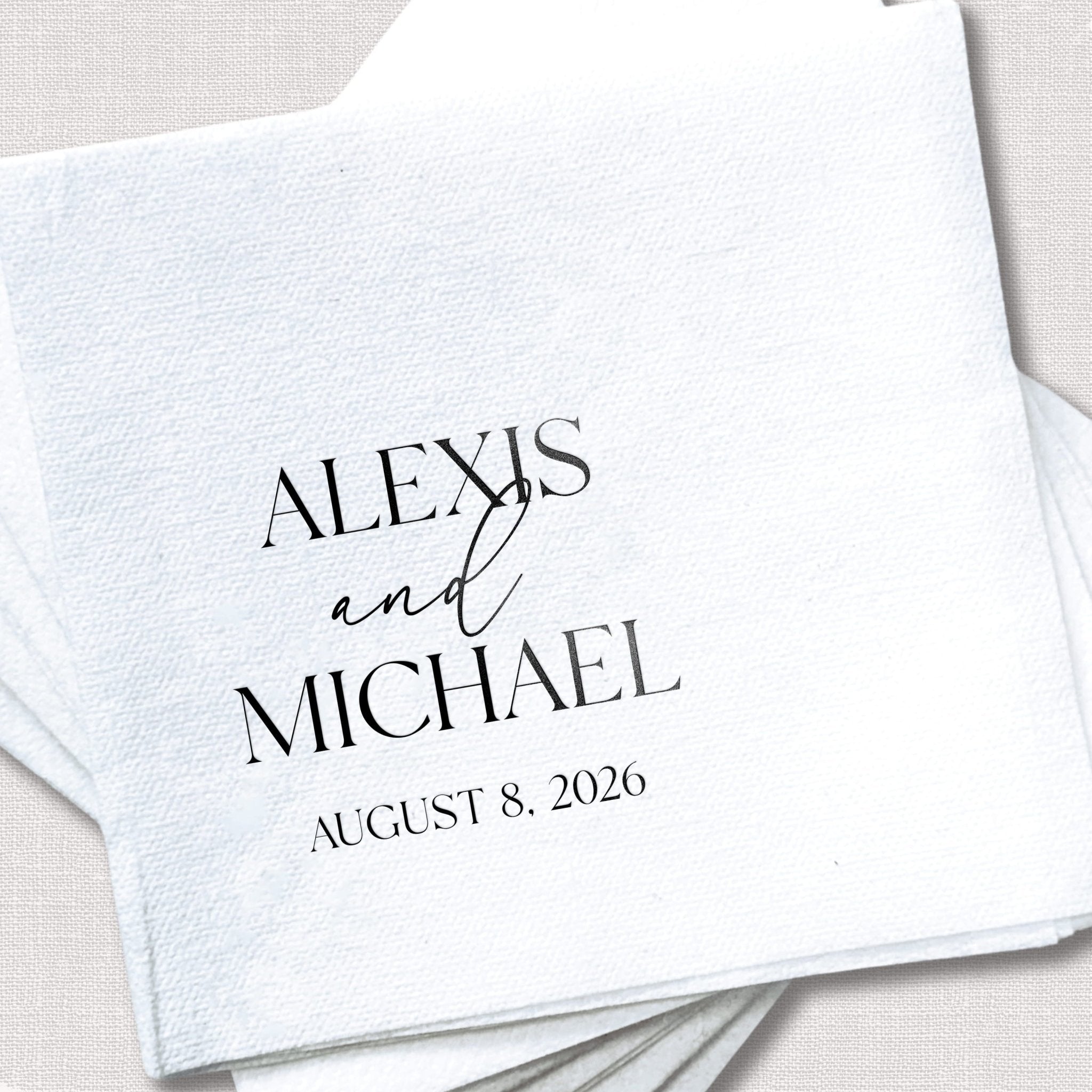 White linen napkin with black text reading "Alexis and Michael, August 8, 2026" personalized wedding design
