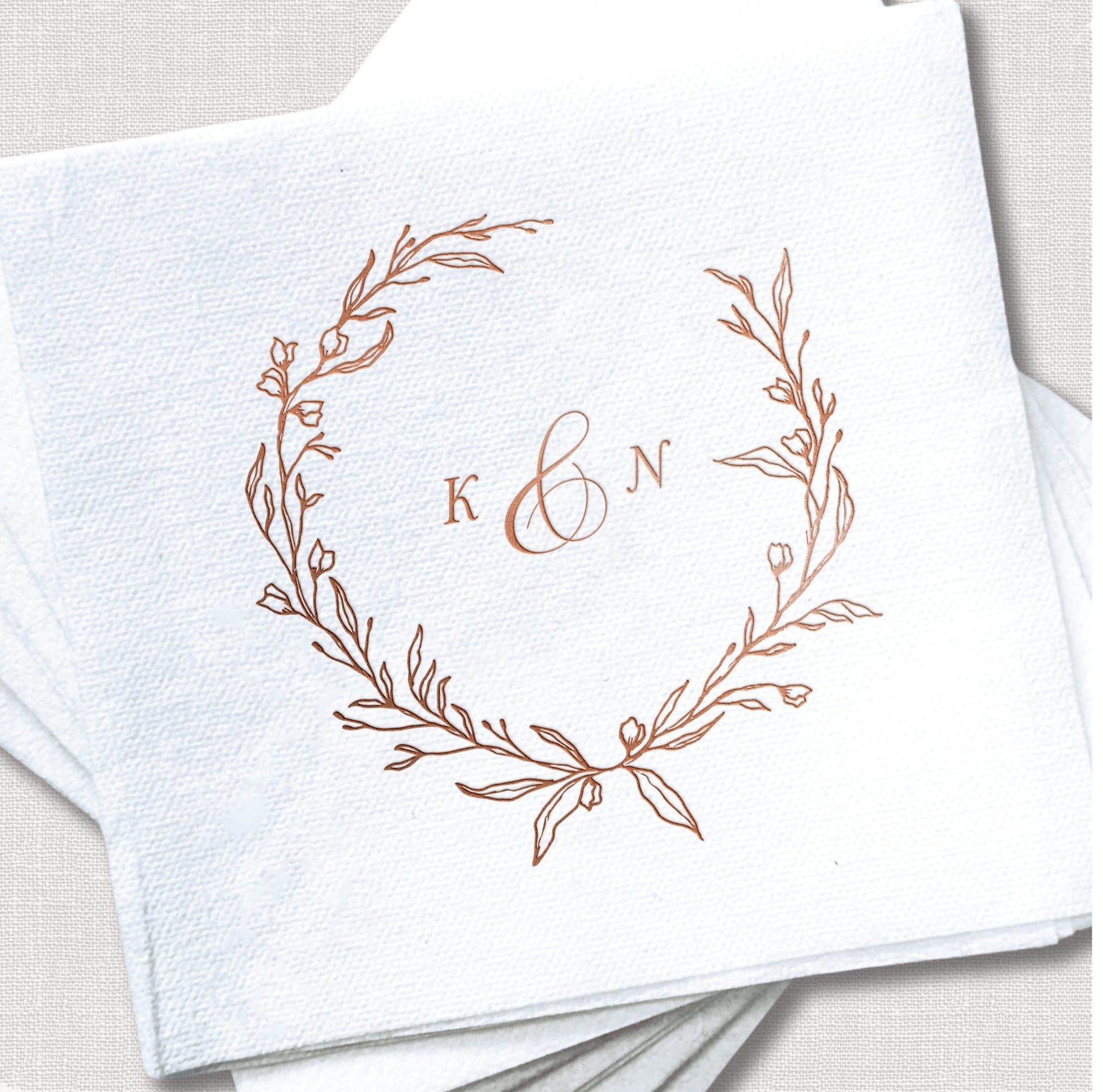 White cocktail napkin with rose gold foil wreath design and initials K and N monogram in center