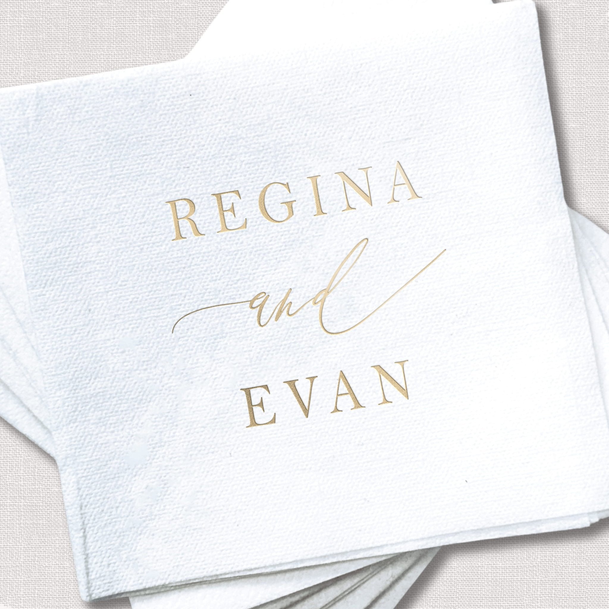 White linen napkins with gold foil stamped names "Regina and Evan" for wedding favors