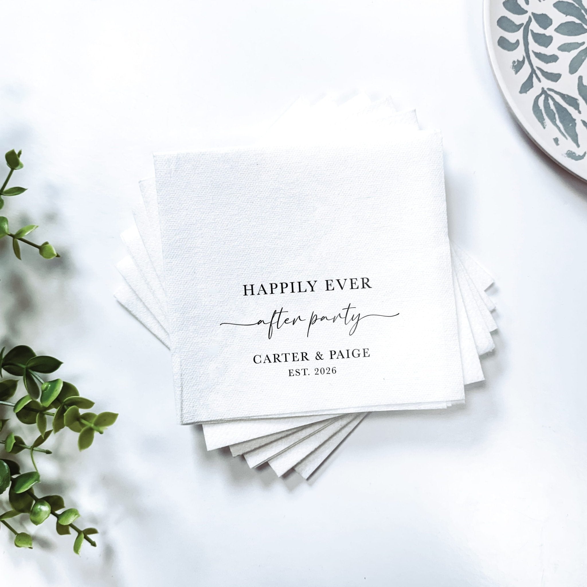Stack of white napkins with "Happily Ever After" and "Carter & Paige EST 2026" printed in black and gold foil text.