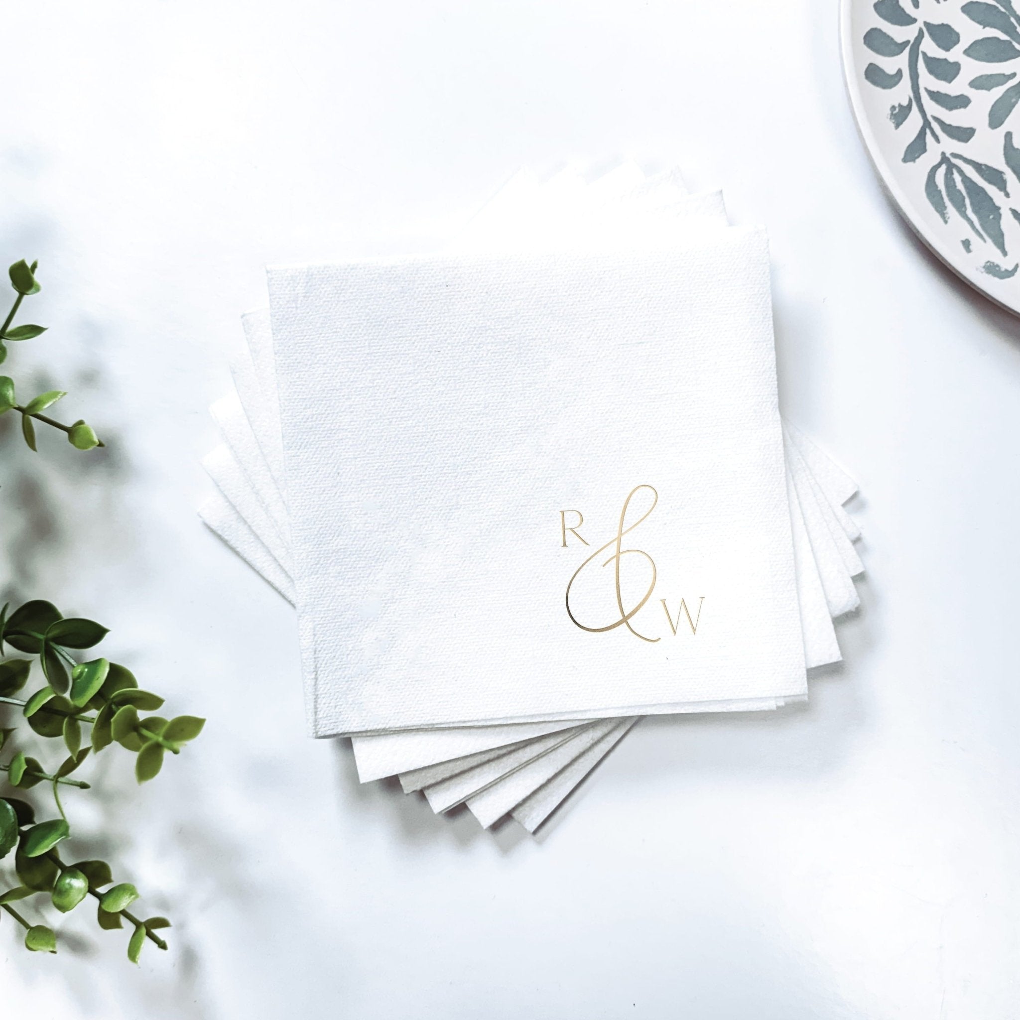 Stack of white linen napkins with gold foil monogram initials and ampersand symbol