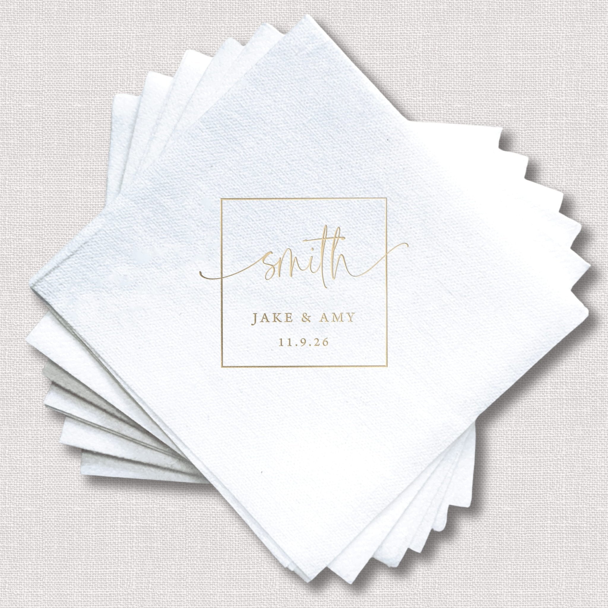 Stack of white linen napkins with gold foil stamped monogram design reading "smith" with "JAKE & AMY 11.9.28" below