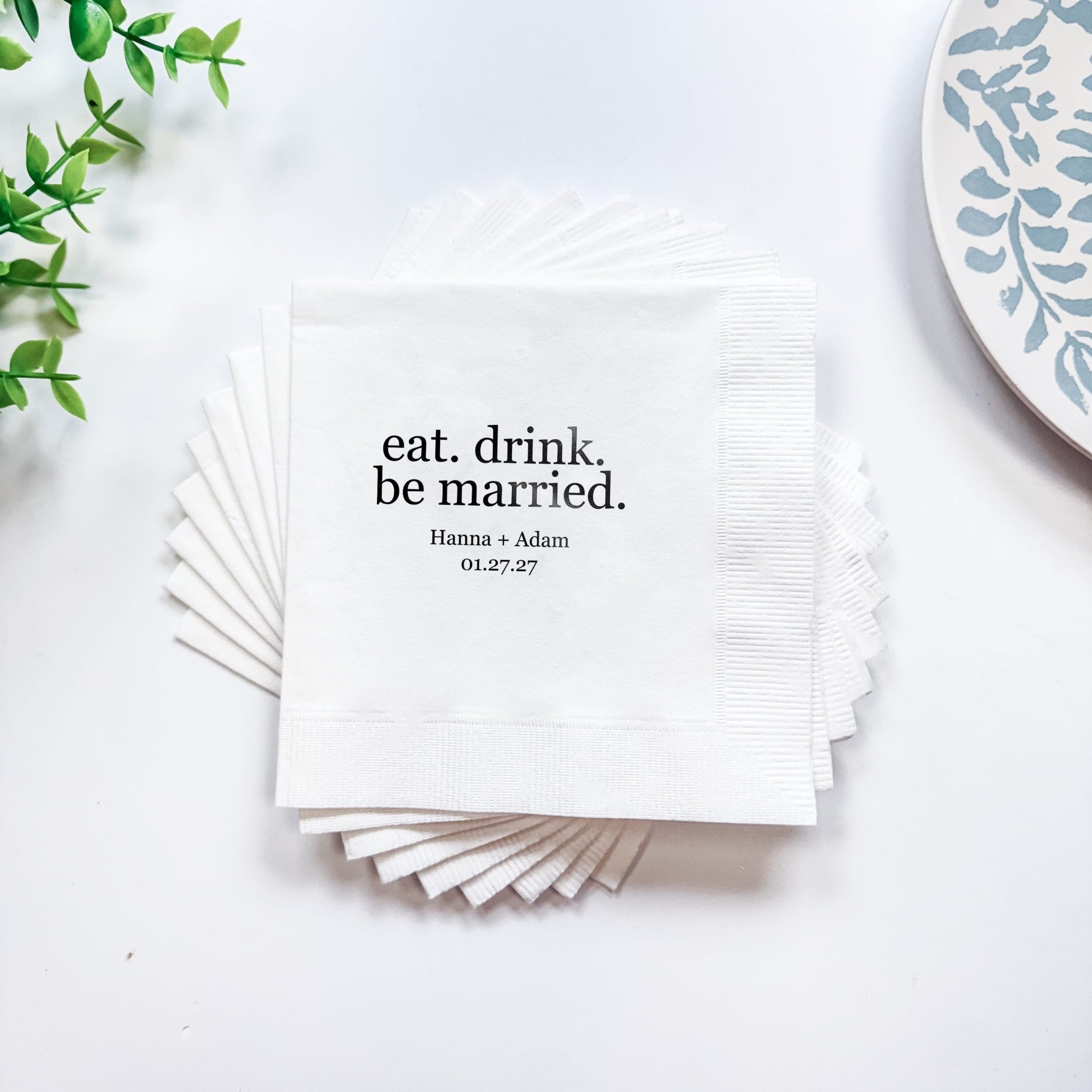 Stack of white napkins with "eat. drink. be married." text and personalized names and date in black foil stamping.