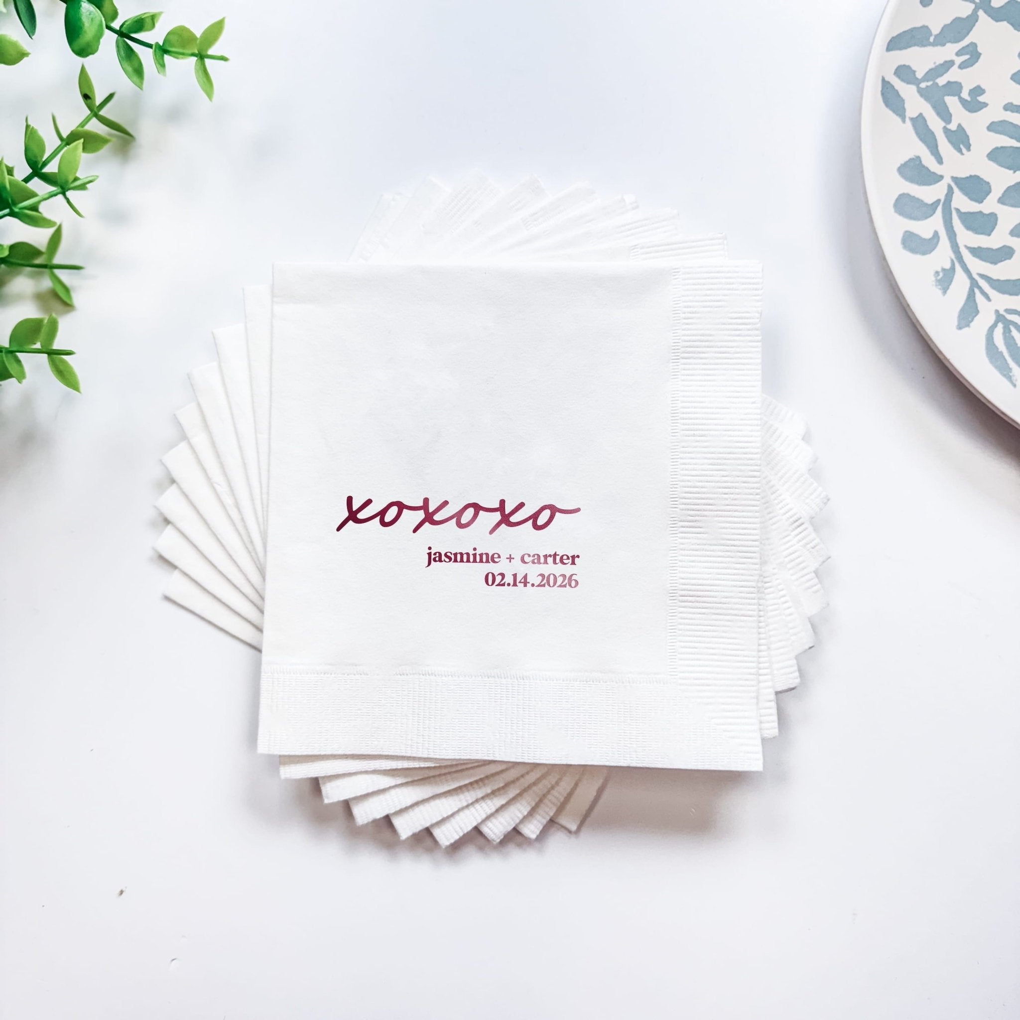 Stack of white napkins with burgundy foil-stamped xoxo design and personalized names with wedding date