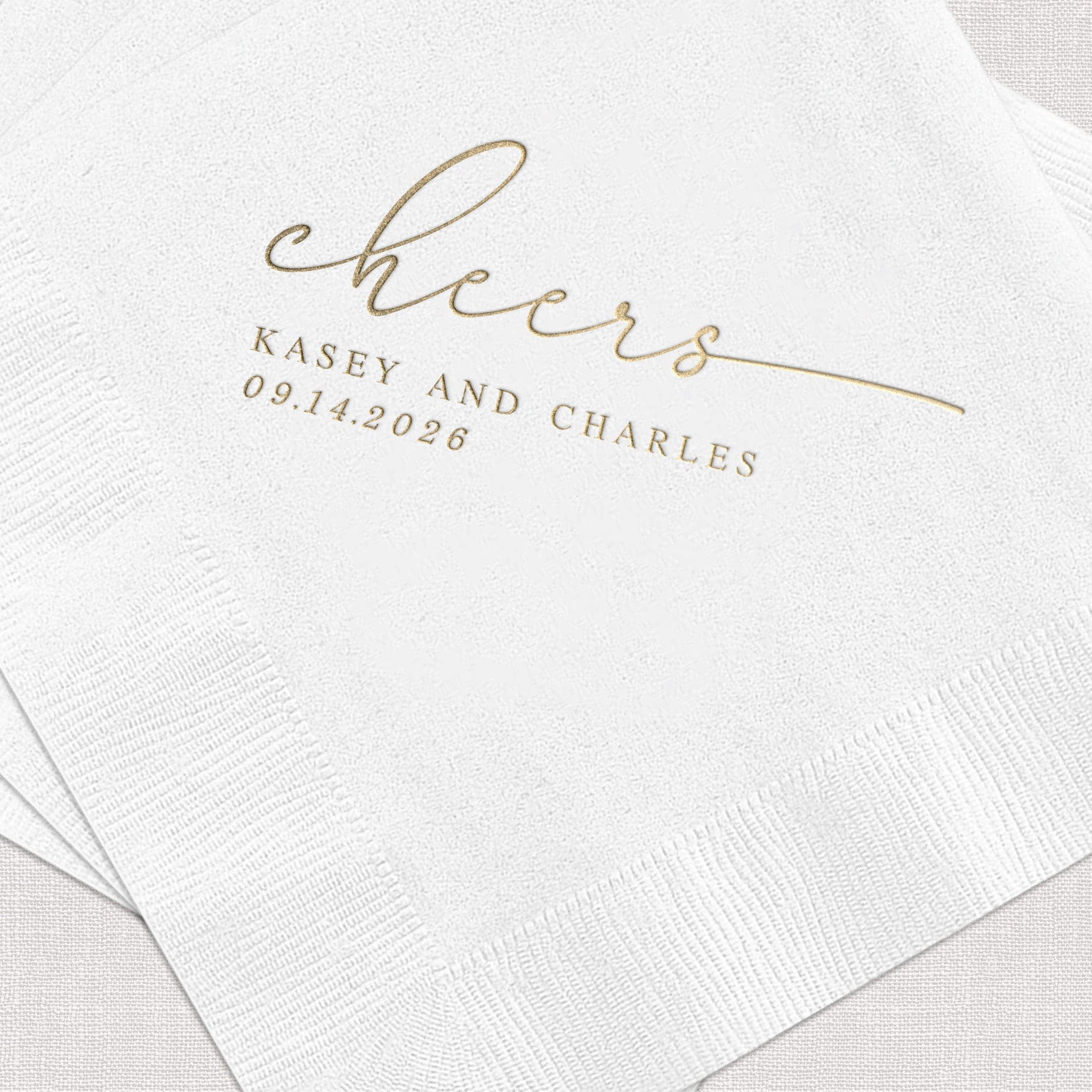 White napkins with gold foil stamped "cheers" script and personalized names Kasey and Charles with wedding date 09.14.2026