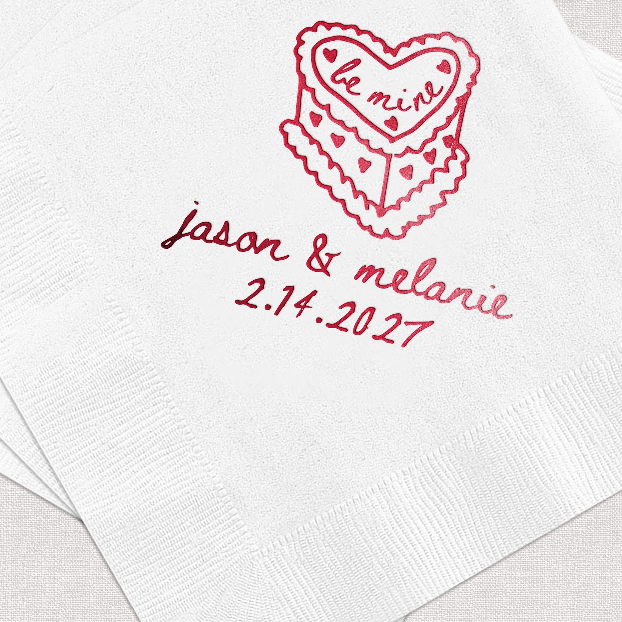 White napkin with red foil-stamped heart design and personalized names "jason & melanie" with wedding date "2.14.2027"