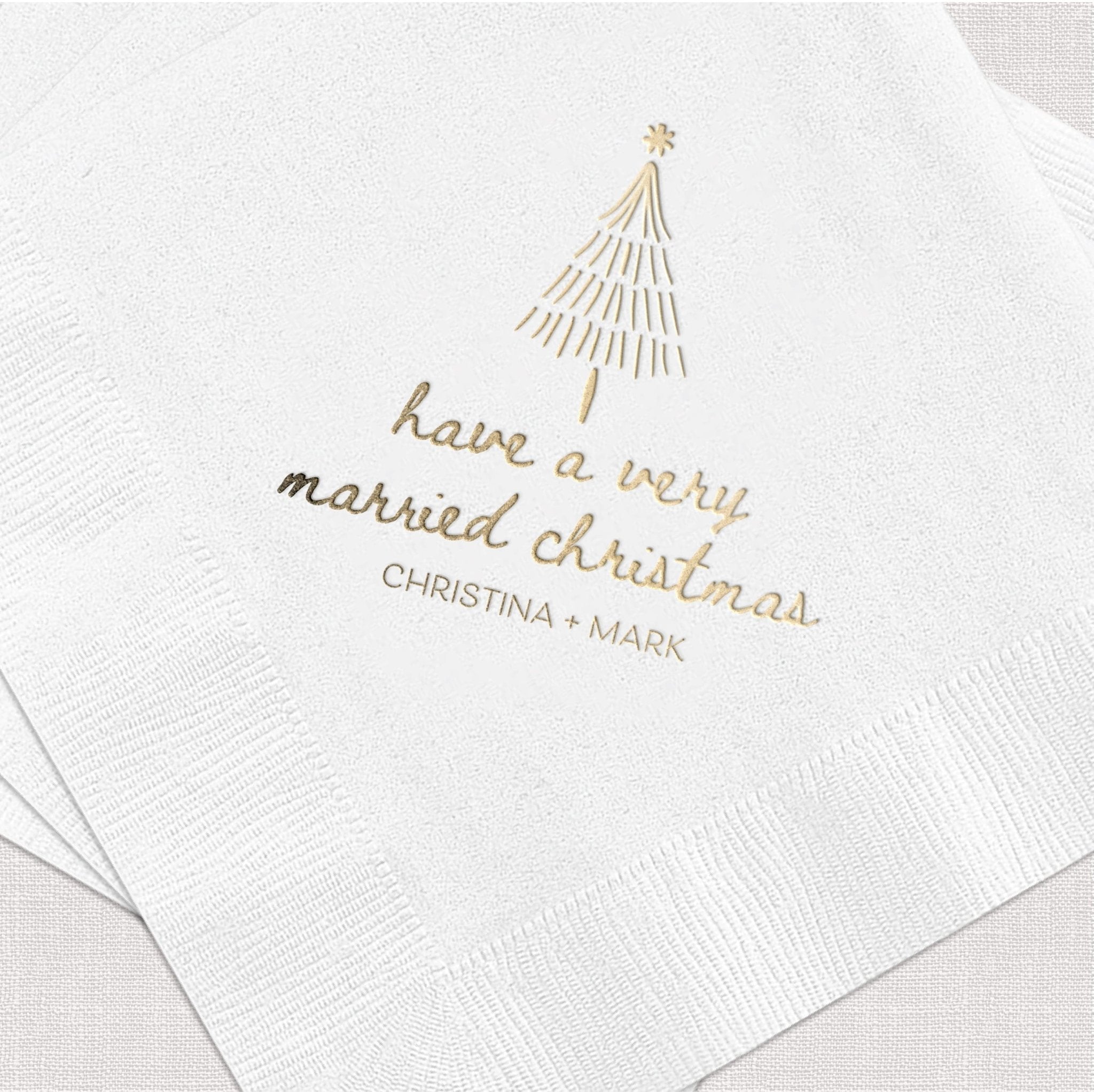 White napkin with gold foil stamped Christmas tree design and "have a very married christmas" text with personalized names below