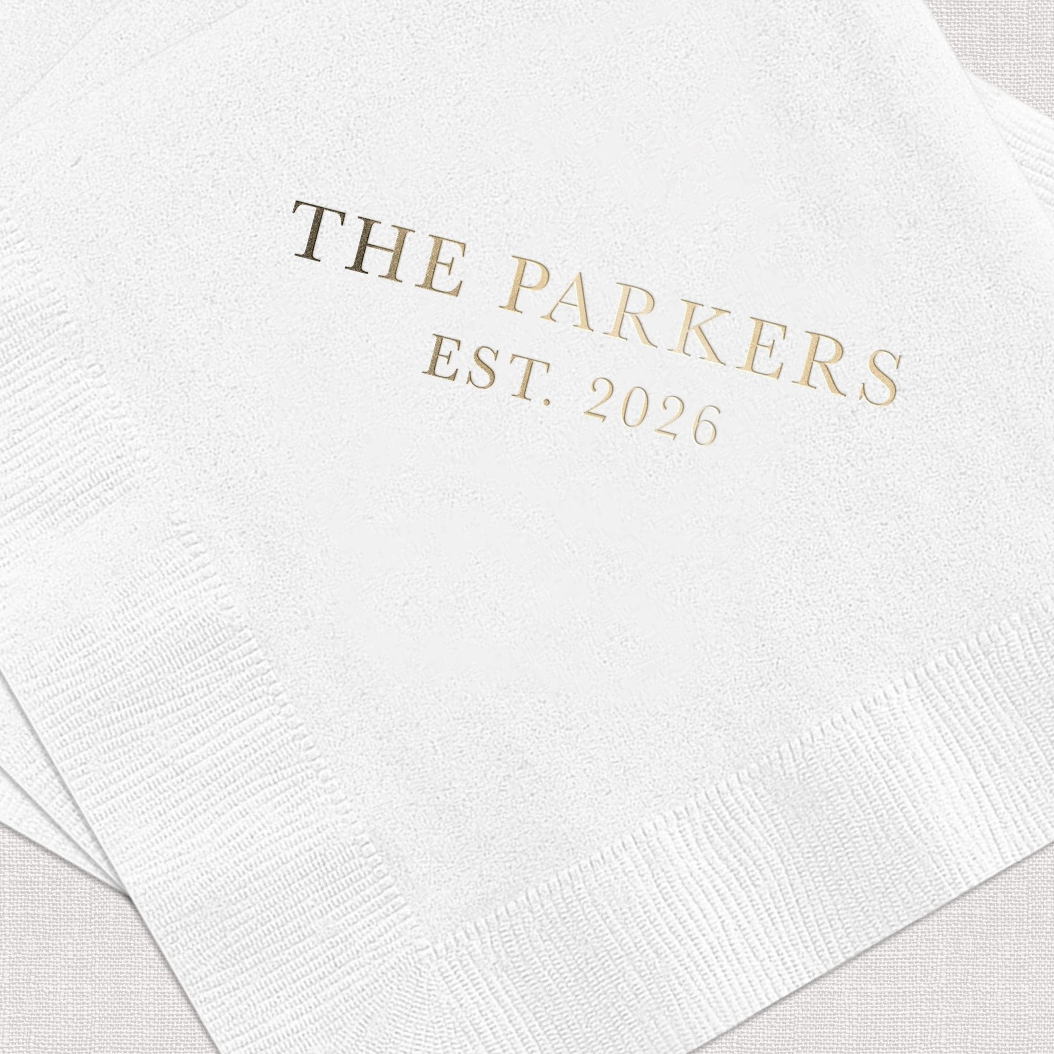 White cocktail napkins with gold foil stamped text reading "THE PARKERS EST. 2026"