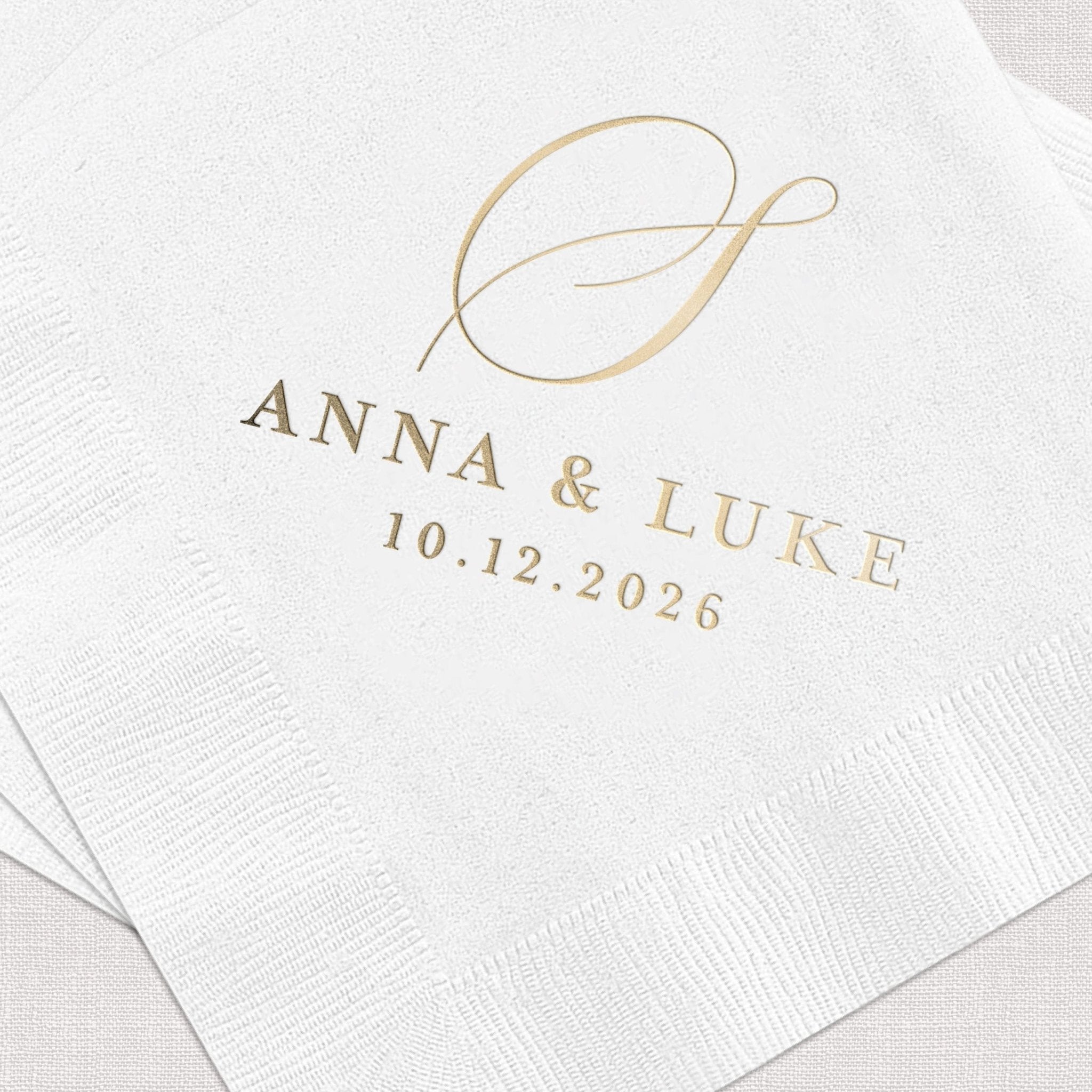 White napkins with gold foil monogram and "Anna & Luke 10.12.2026" wedding date text