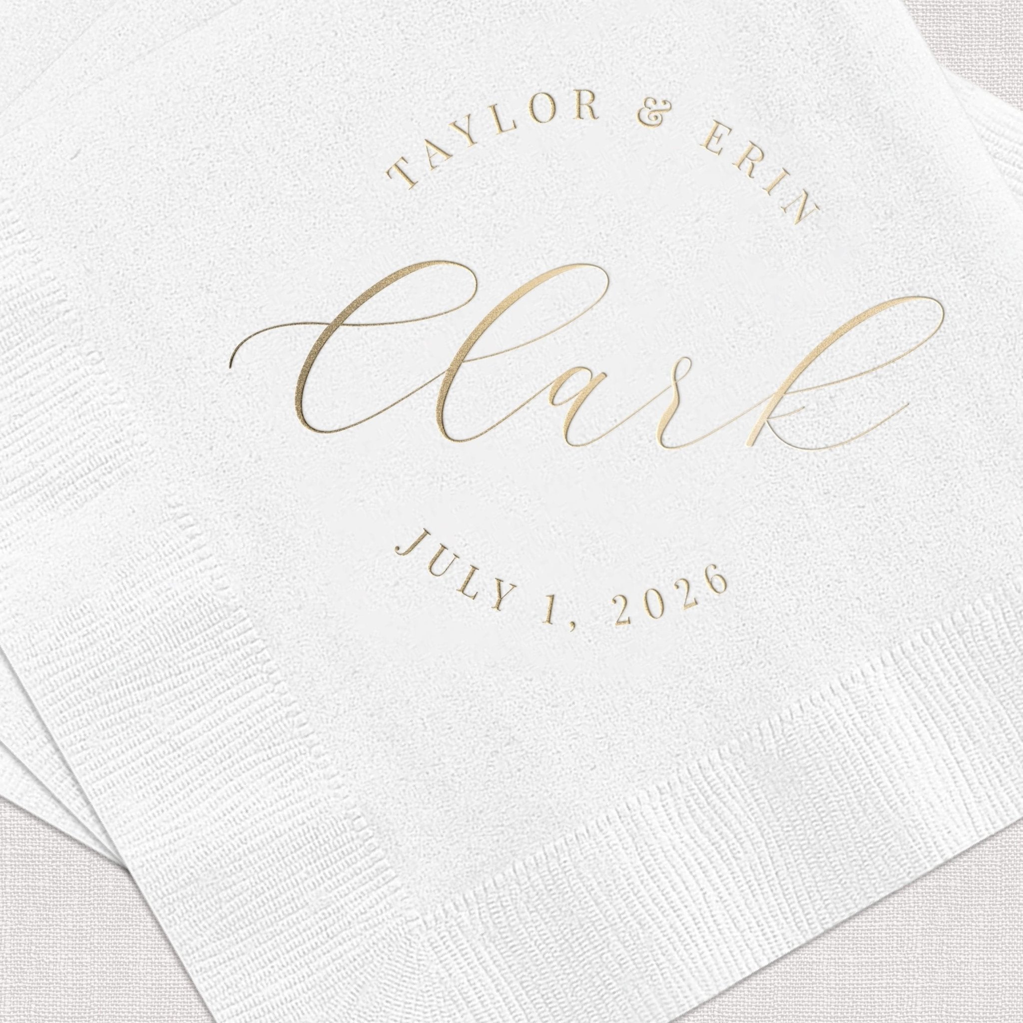 White cocktail napkins with gold foil stamped text reading "TAYLOR & BRIT Clark JULY 1, 2026"
