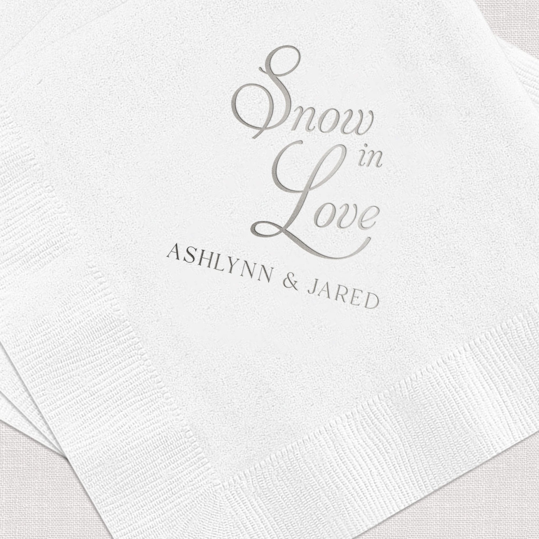 White napkin with gray foil-stamped text reading "Snow in Love" and "ASHLYNN & JARED" personalization