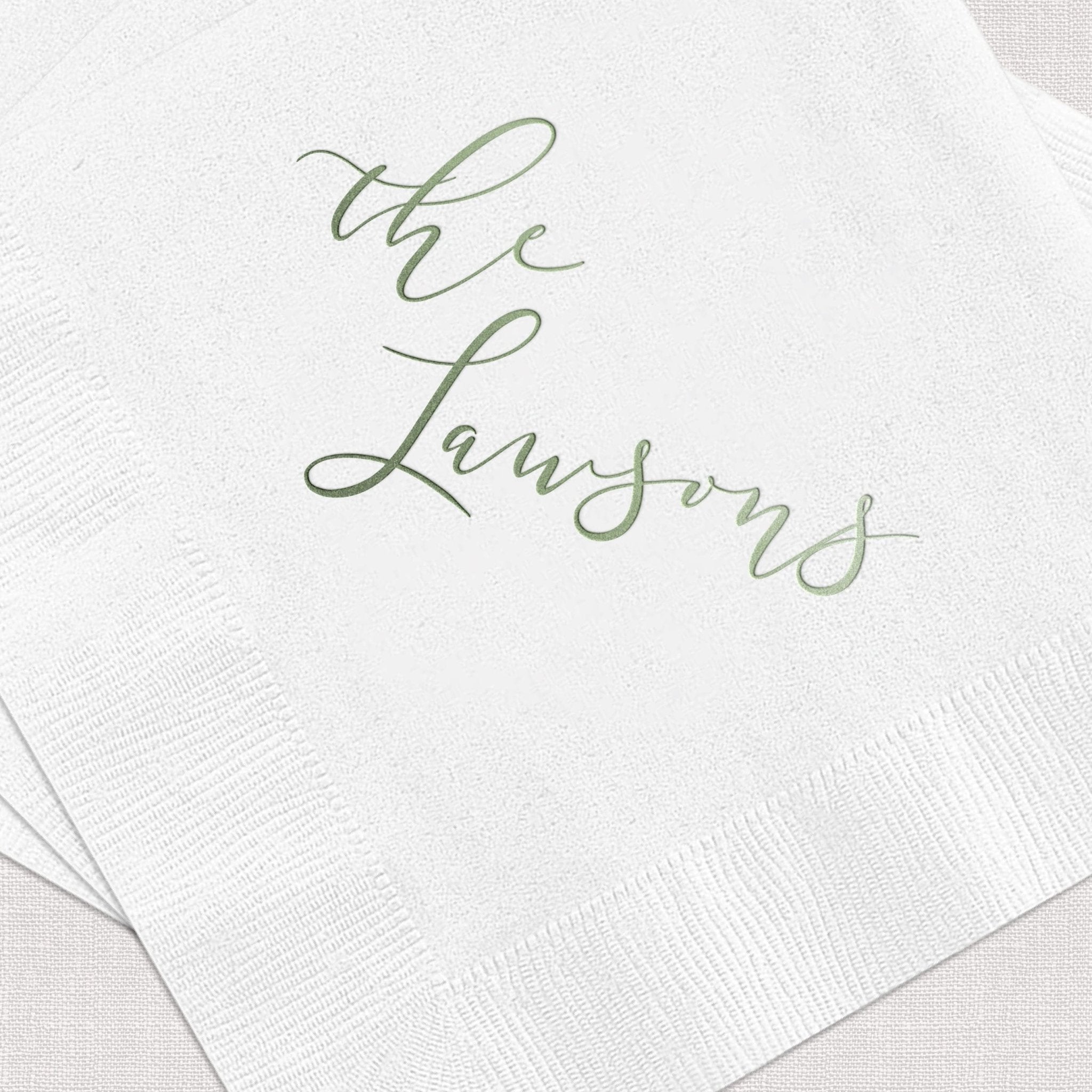White napkins with sage green foil-stamped script reading "the Lansons" in elegant cursive lettering.