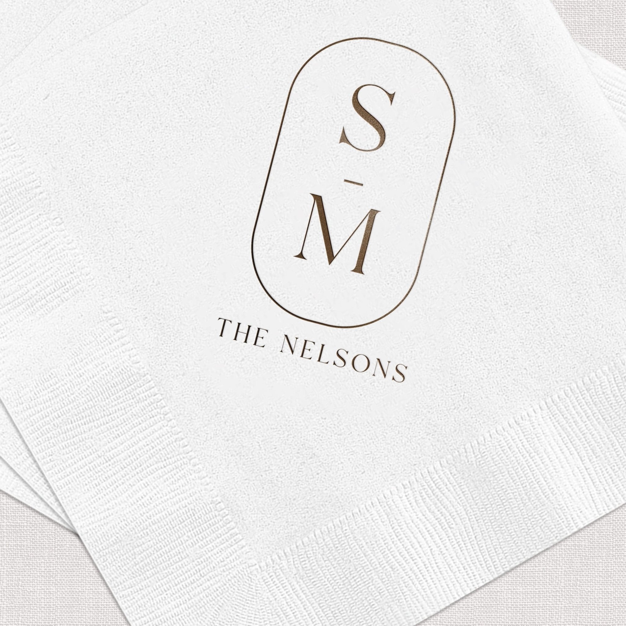 White napkin with foil-stamped initials S and M with "The Nelsons" text below in elegant serif font.