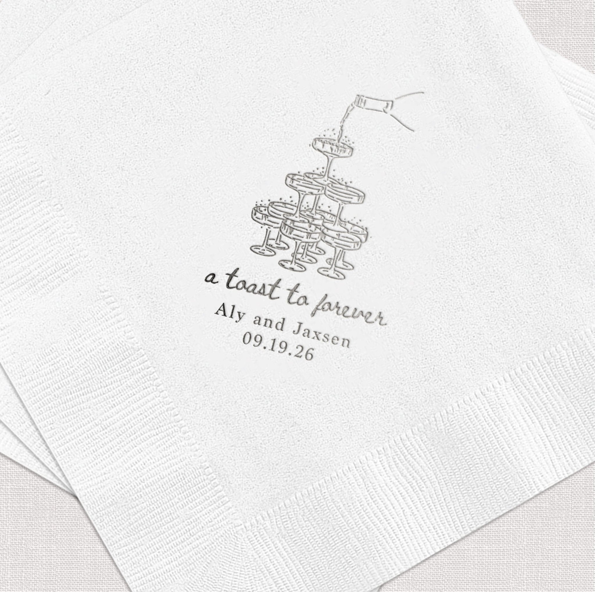 White napkin with silver foil-stamped champagne glasses and "a toast to forever" text with names Aly and Jaxen and date 09.19.26