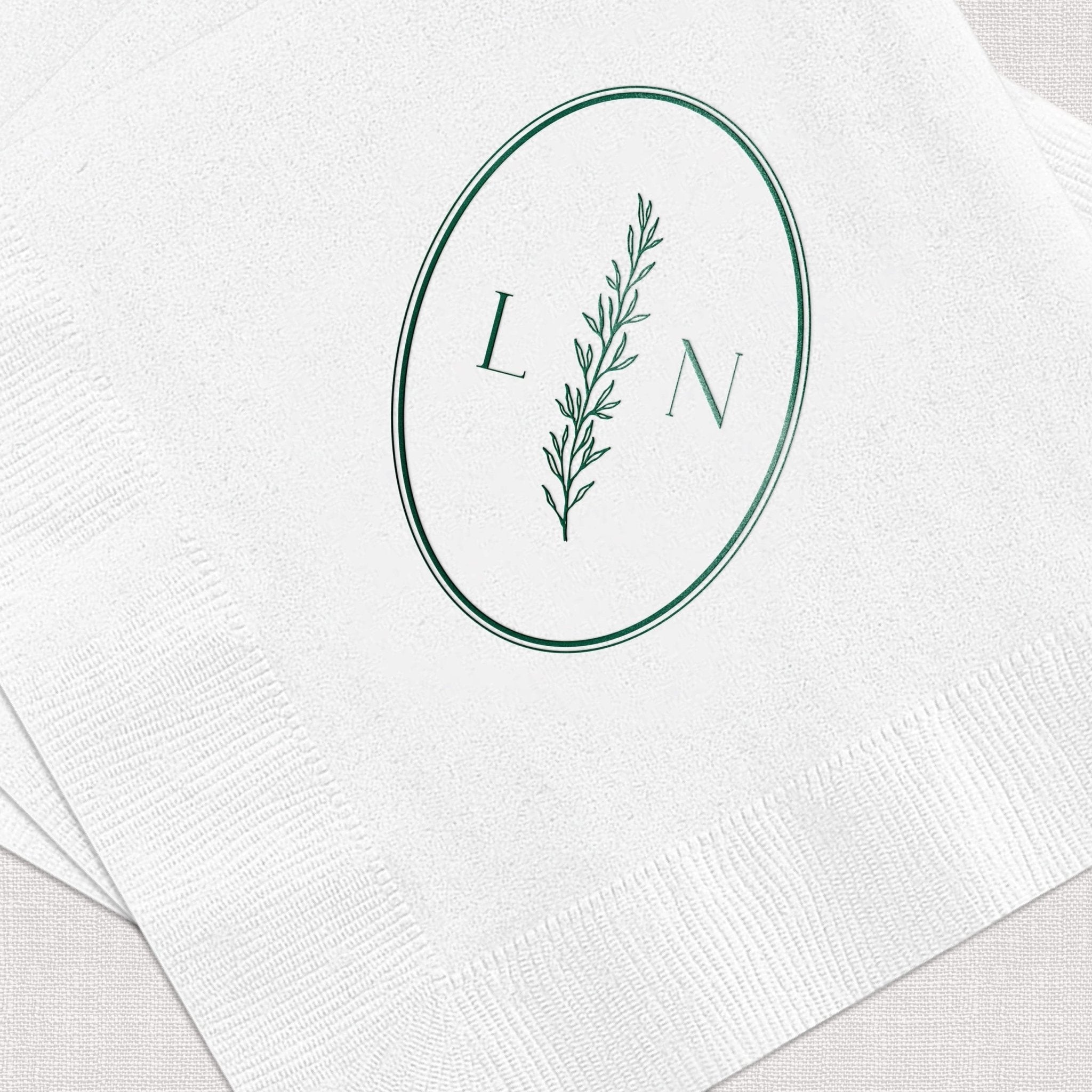 White cocktail napkins with teal foil-stamped oval frame, botanical branch, and initials L and N.