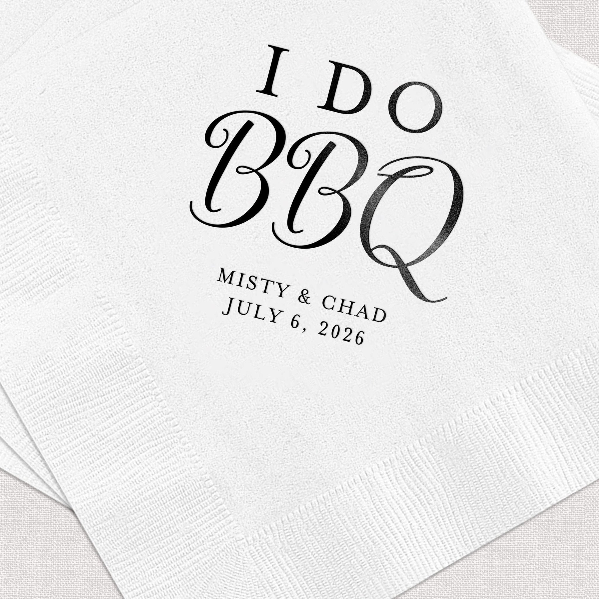 White napkin with black foil-stamped text reading "I DO BBQ" and personalized names "MISTY & CHAD" with wedding date "JULY 6, 2026"