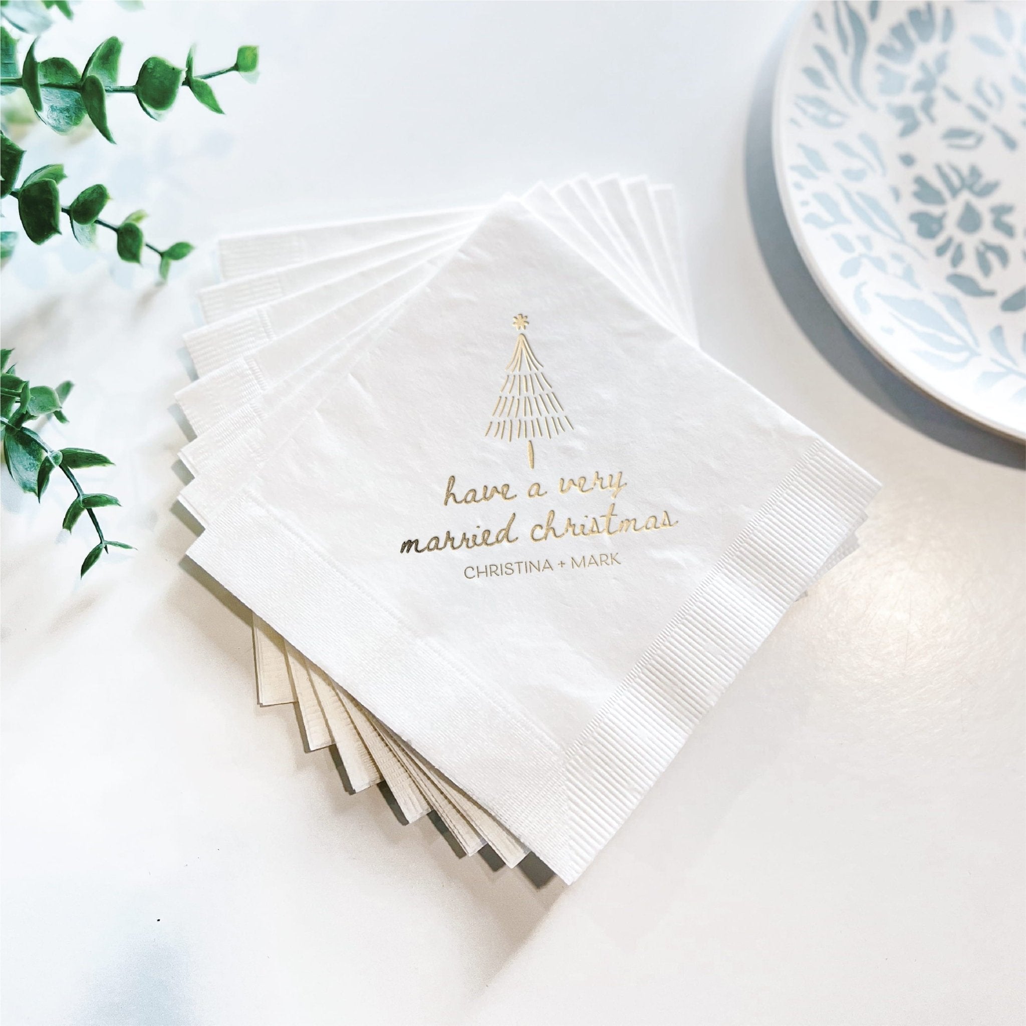 Stack of white napkins with gold foil Christmas tree and "have a very married christmas" text design