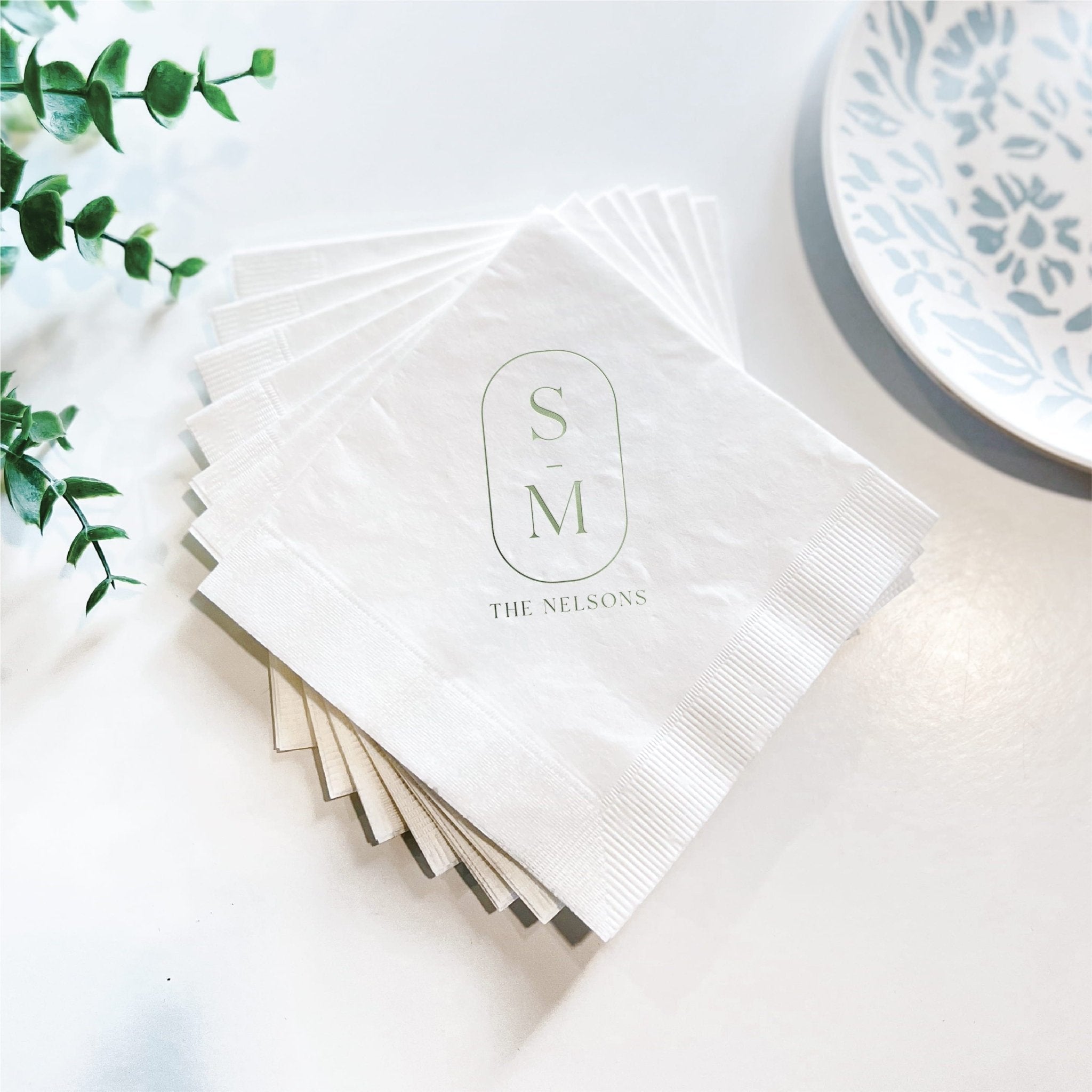 Stack of white napkins personalized with monogram S M and "The Nelsons" text in foil stamped design