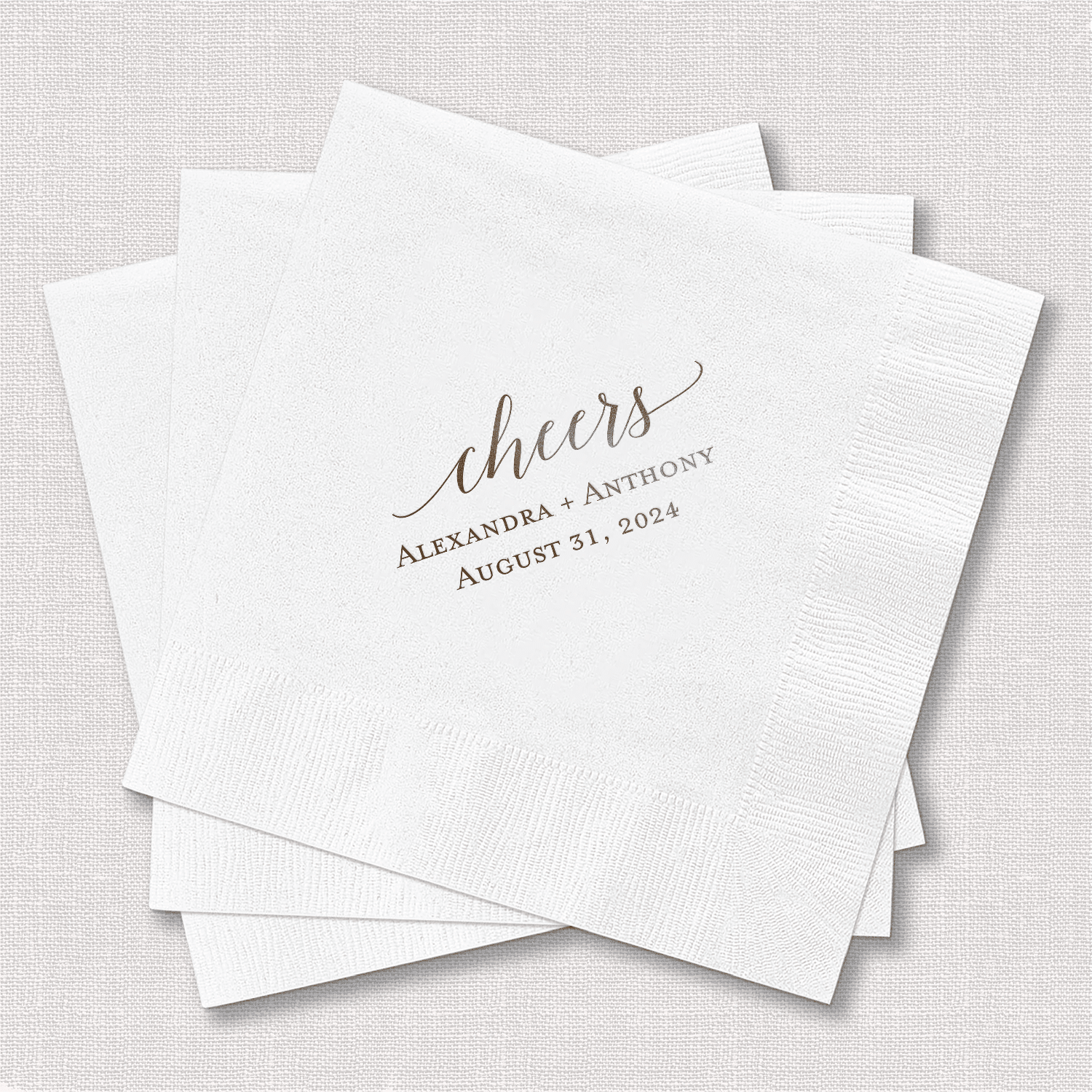 White foil-stamped cocktail napkins with "cheers" script and personalized names and wedding date in gold lettering.