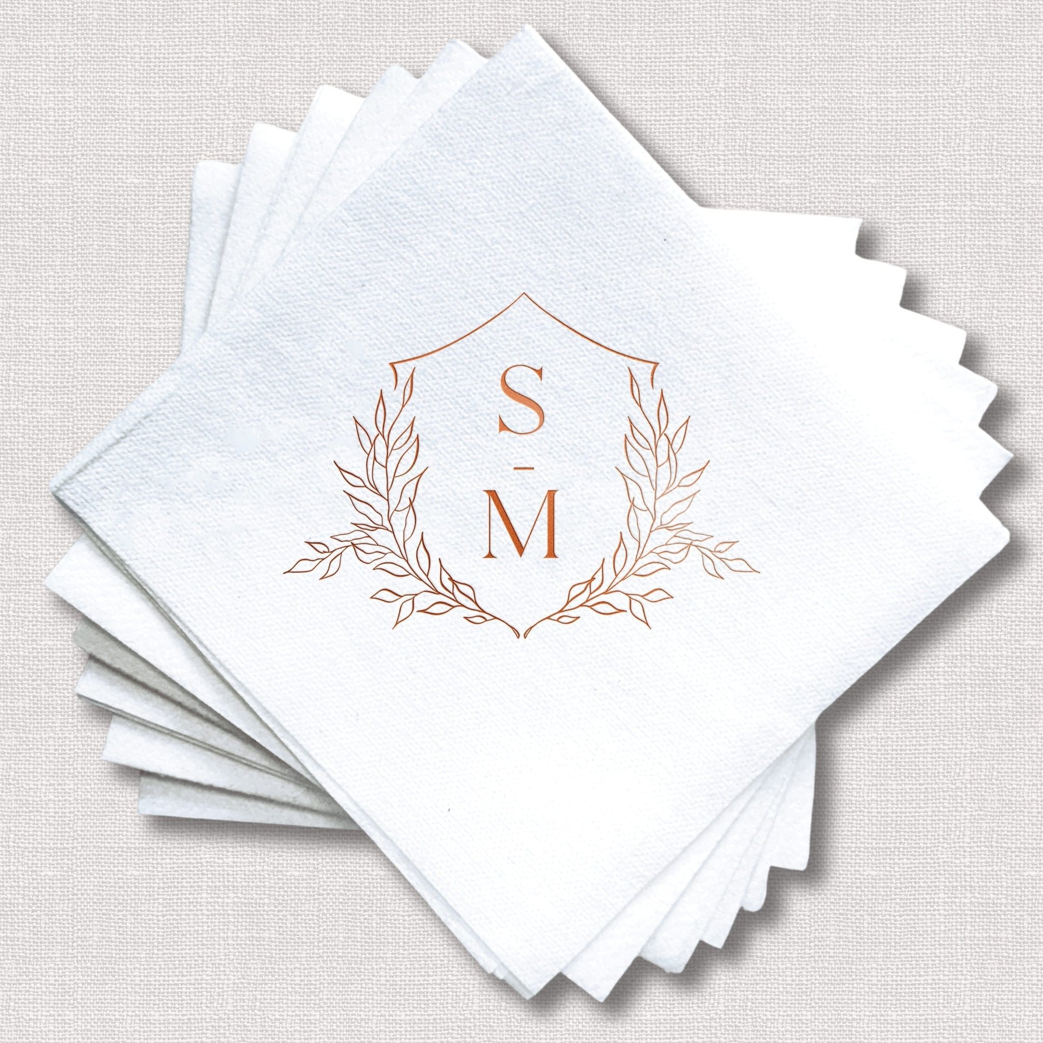 Stack of white linen napkins with rose gold foil stamped floral crest monogram featuring initials S and M.