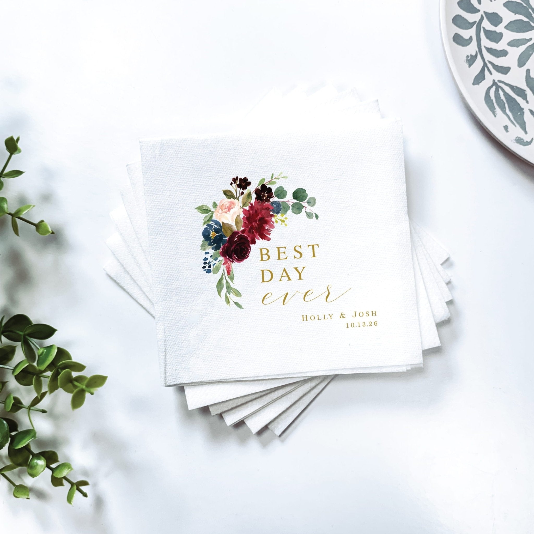 Stack of white napkins with burgundy floral design and gold "Best Day Ever" text with personalized names and date