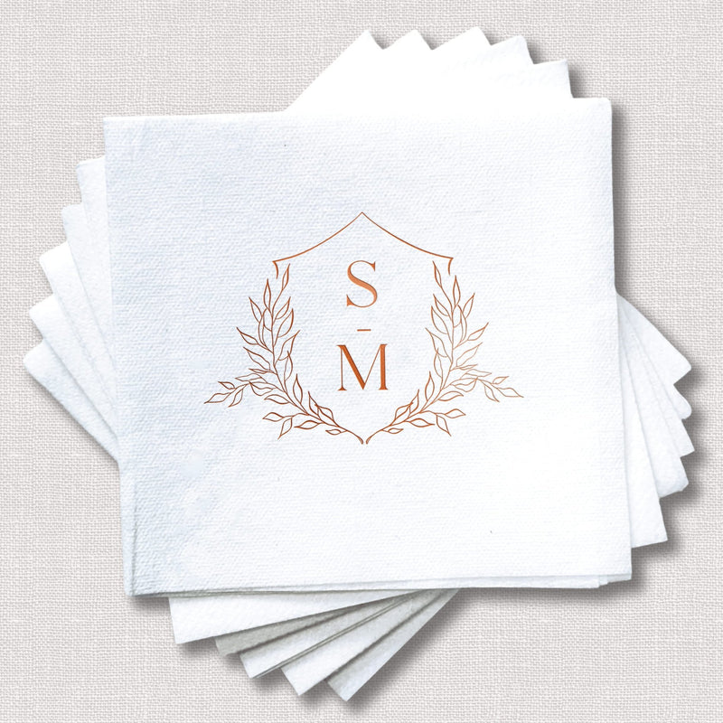 Stack of white linen napkins with copper foil stamped floral crest monogram featuring initials S and M.