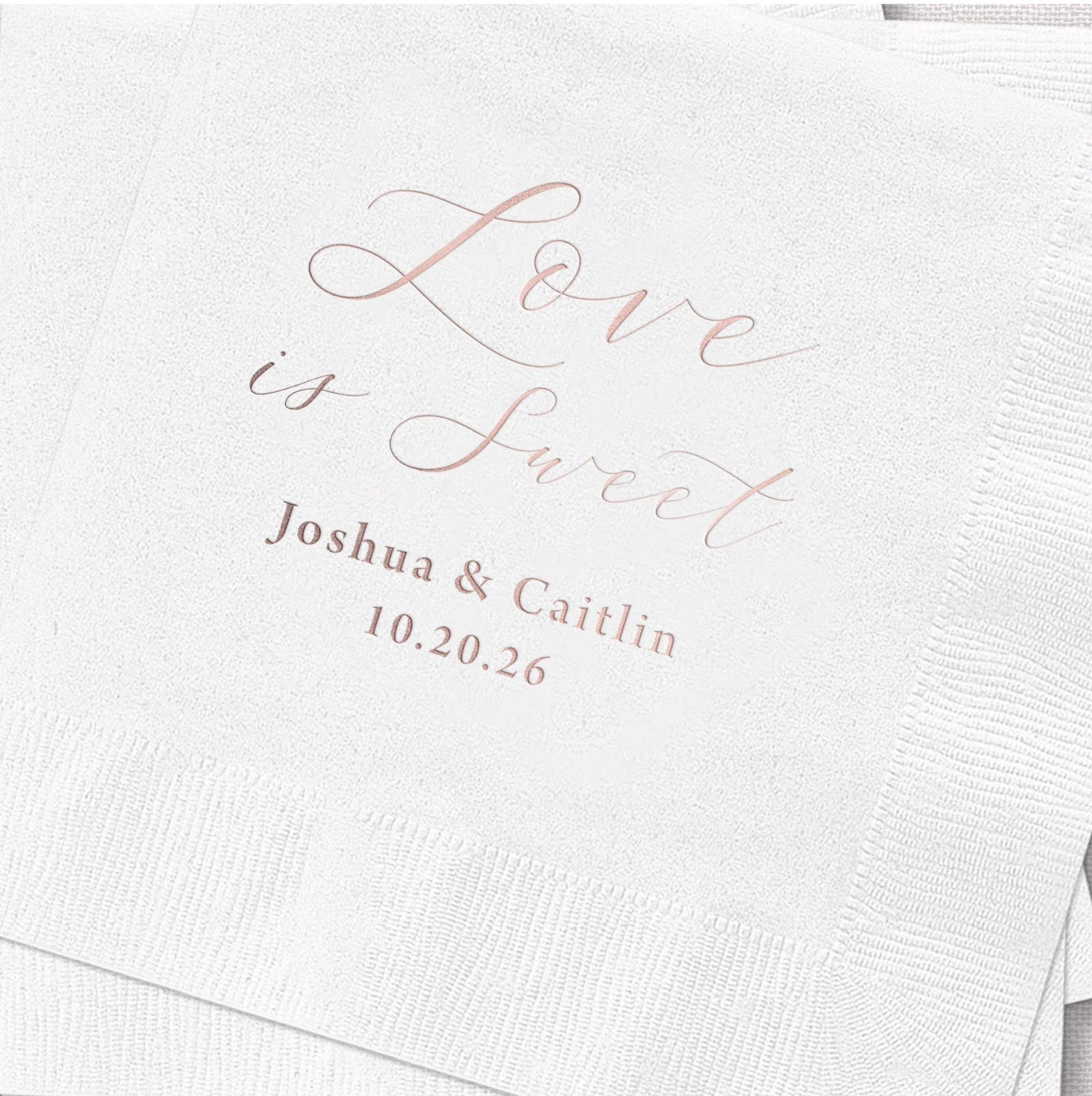 White napkin with rose gold foil stamped text reading "Love is Sweet" and personalized names "Joshua & Caitlin" with wedding date 10.20.26