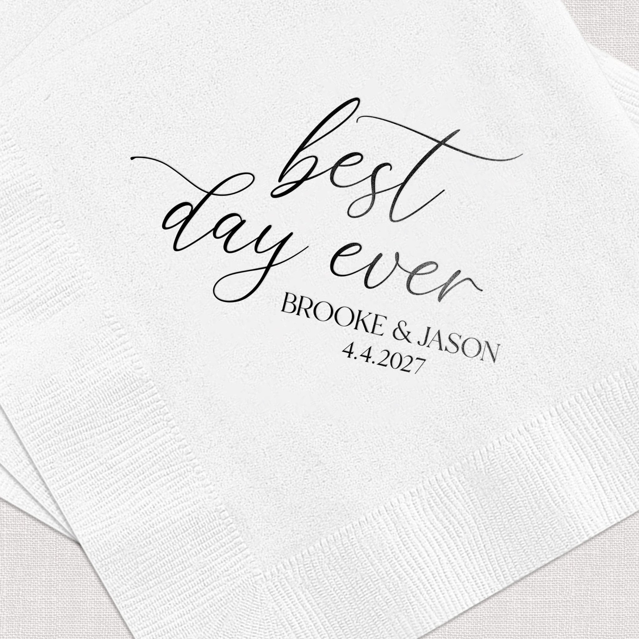White cocktail napkins with "best day ever" in script and "BROOKE & JASON 4.4.2027" in black foil stamping