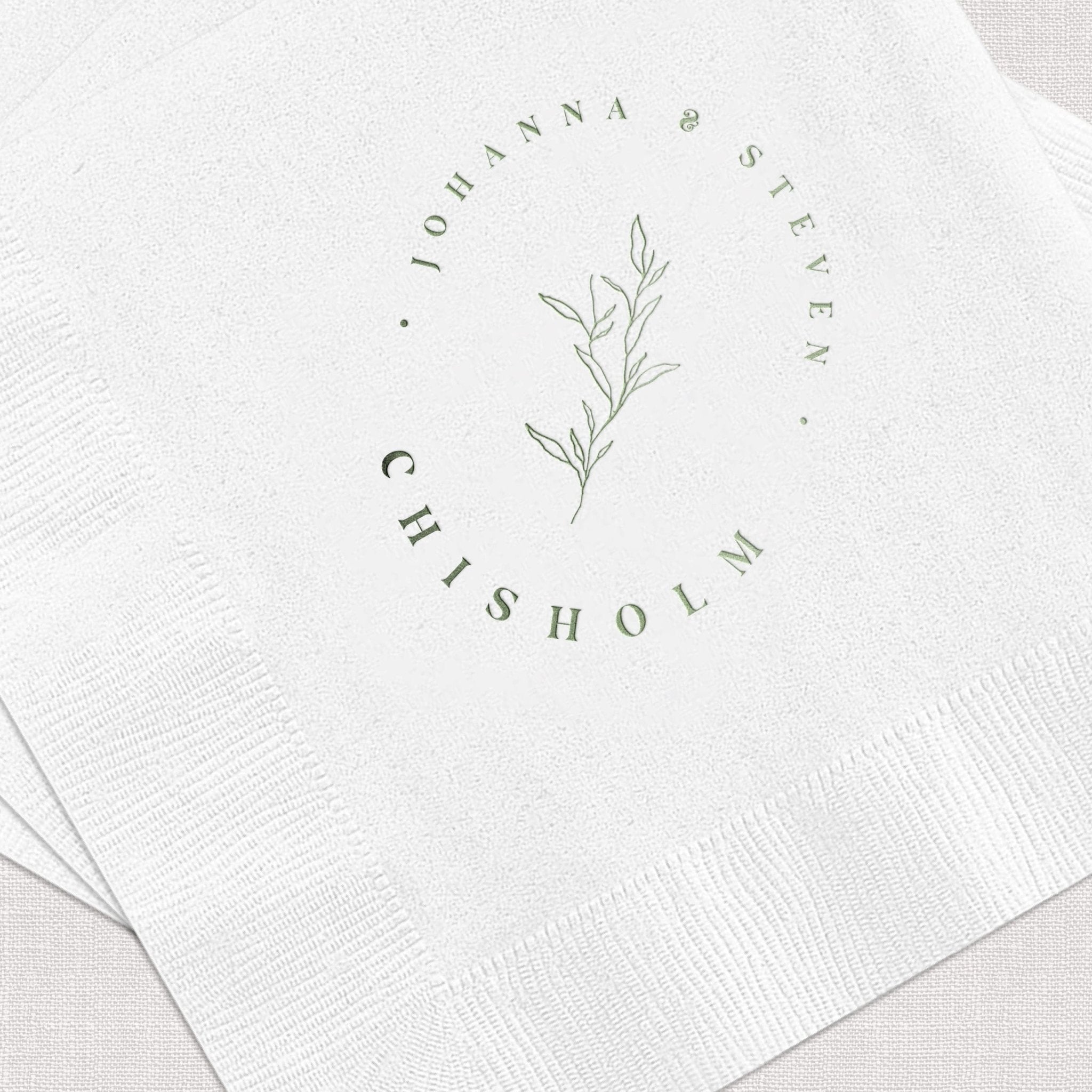 White napkin with sage foil-stamped circular design featuring names Johanna and Steven with botanical leaf illustration and "Chisholm" text.
