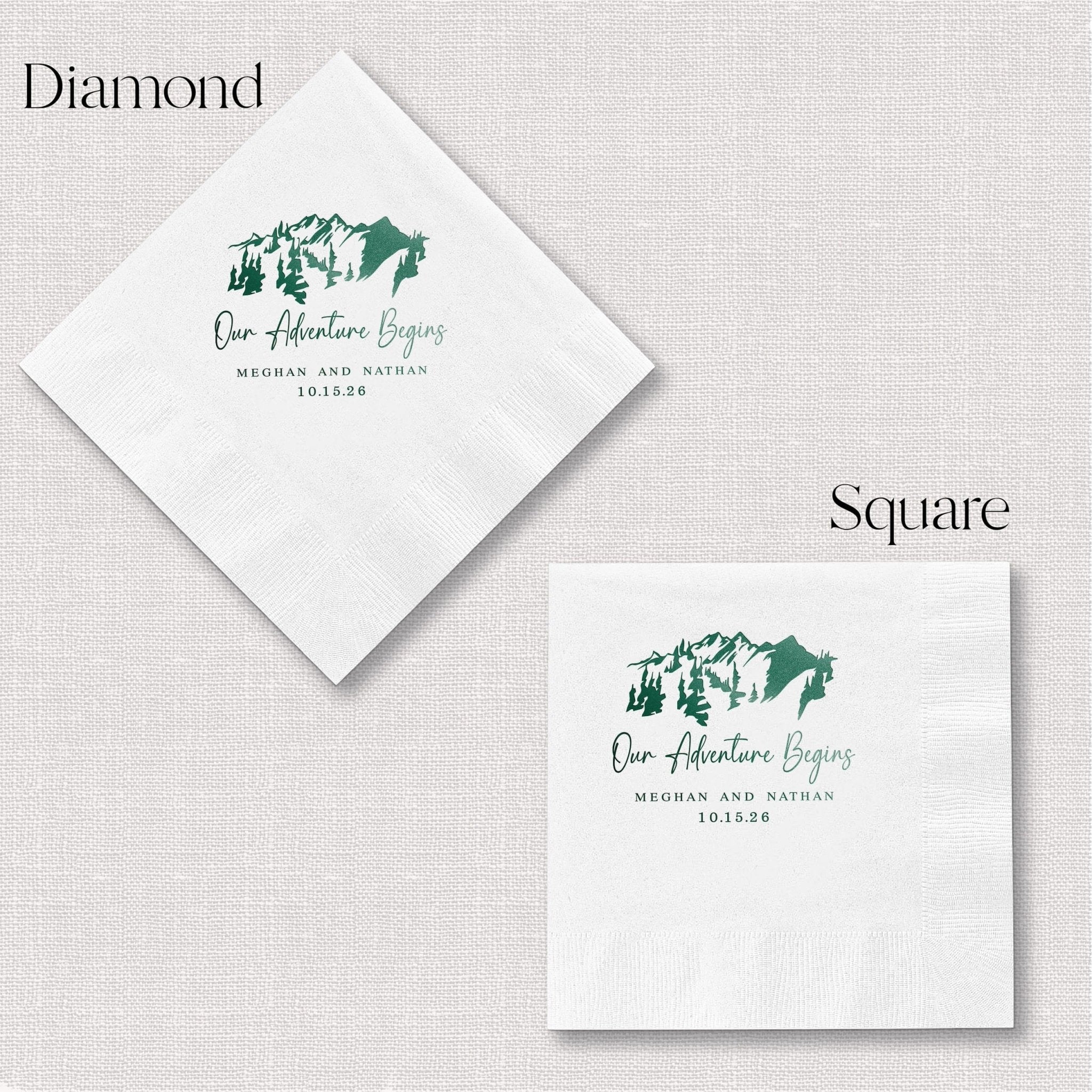 White napkins in diamond and square shapes with green foil-stamped mountain design and "Our Adventure Begins" text with wedding date.