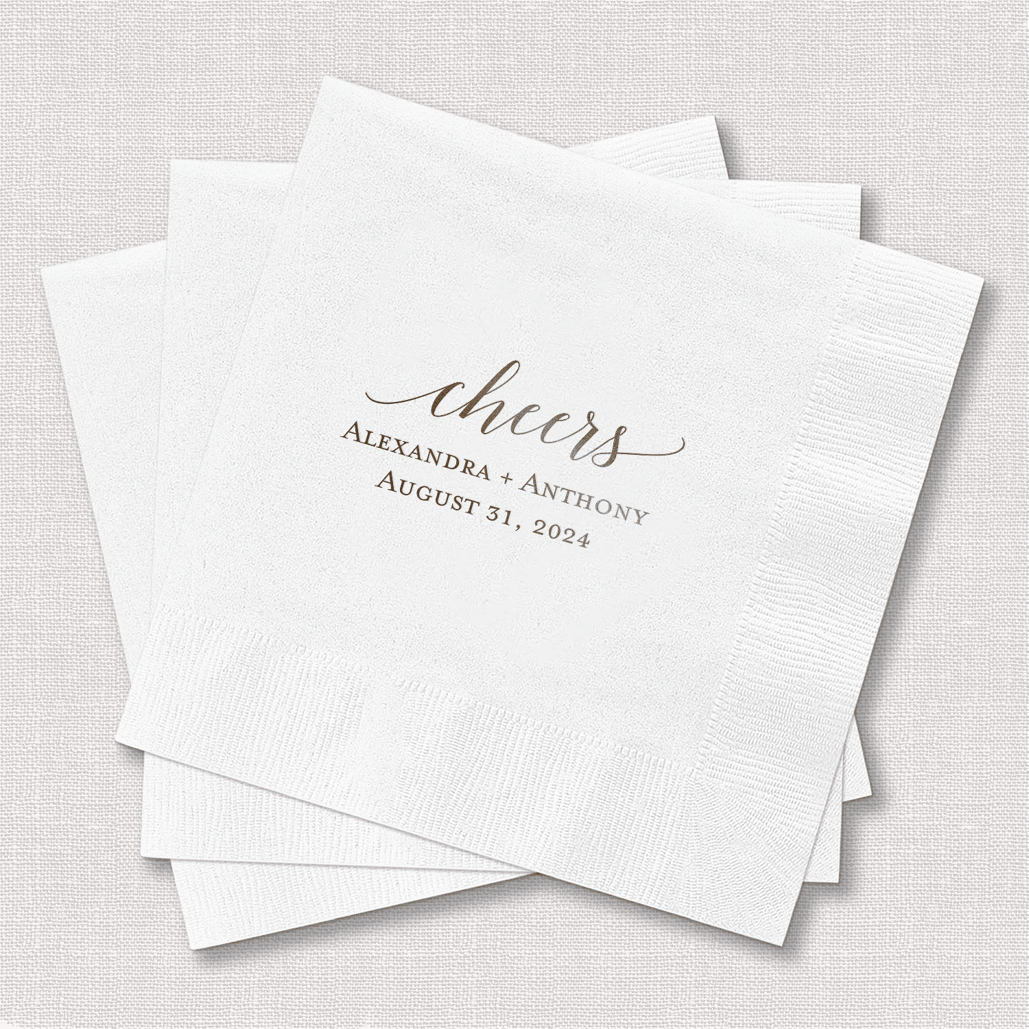 Stack of white foil-stamped cocktail napkins with "cheers" and personalized names and wedding date.