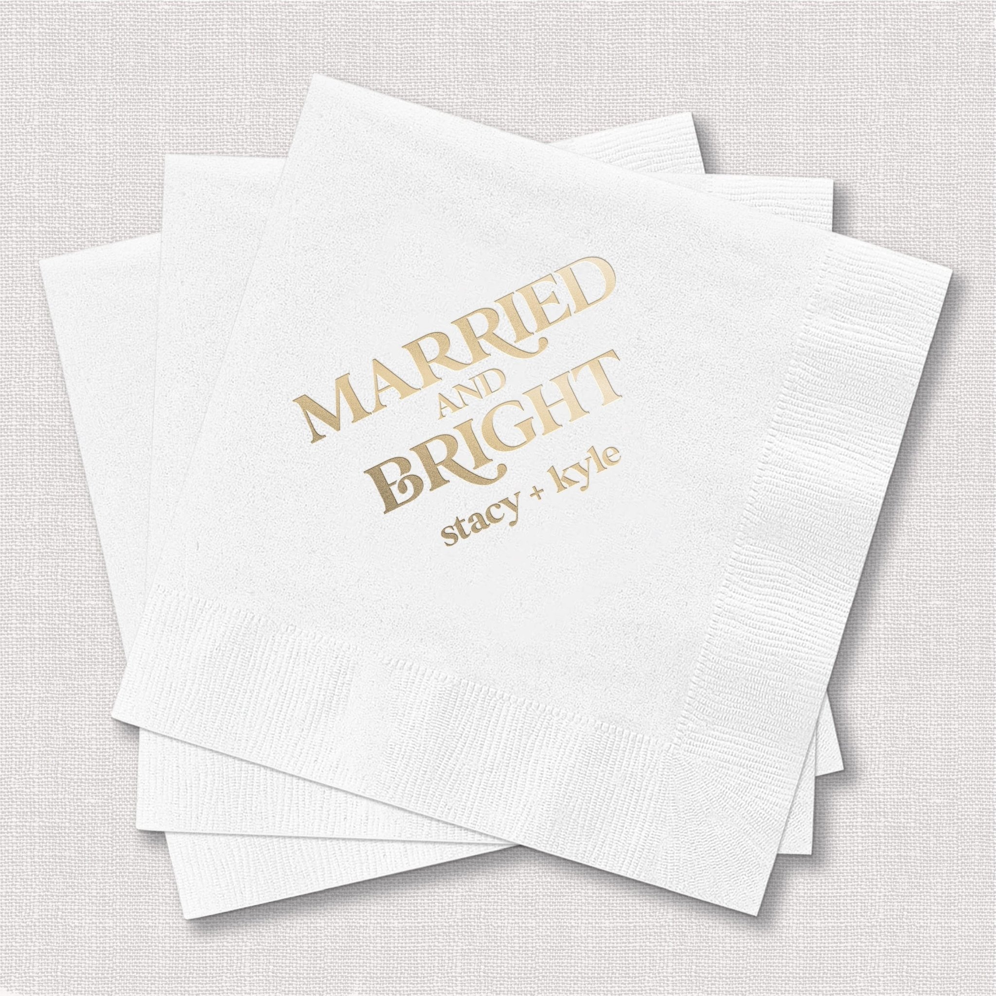 Stack of white personalized napkins with gold foil text reading "Married And Bright" and custom names, wedding favor napkins.