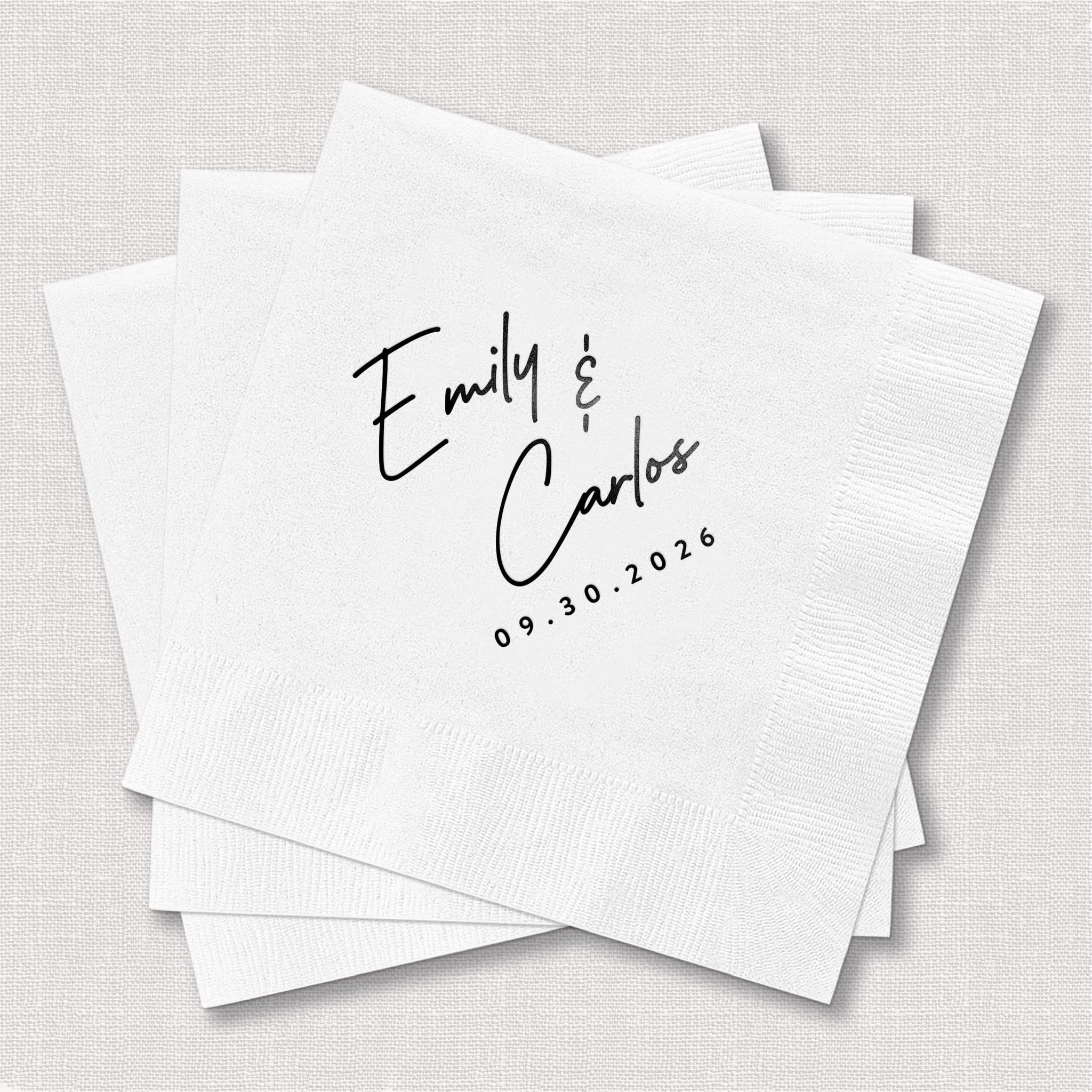 White cocktail napkins personalized with "Emily & Carlos" handwritten script and date 09.30.2026