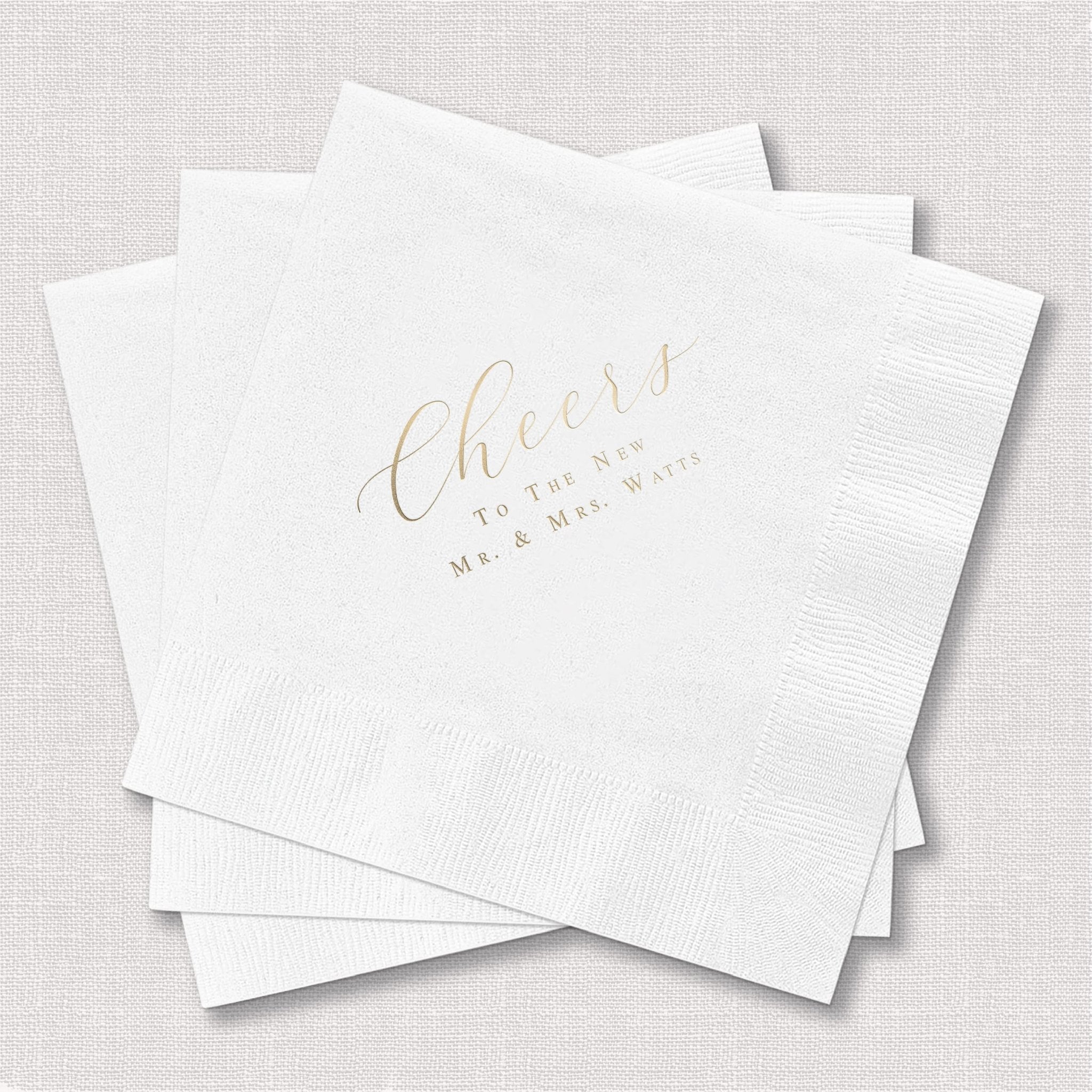 Stack of white cocktail napkins with gold foil "cheers" text and personalized wedding date details