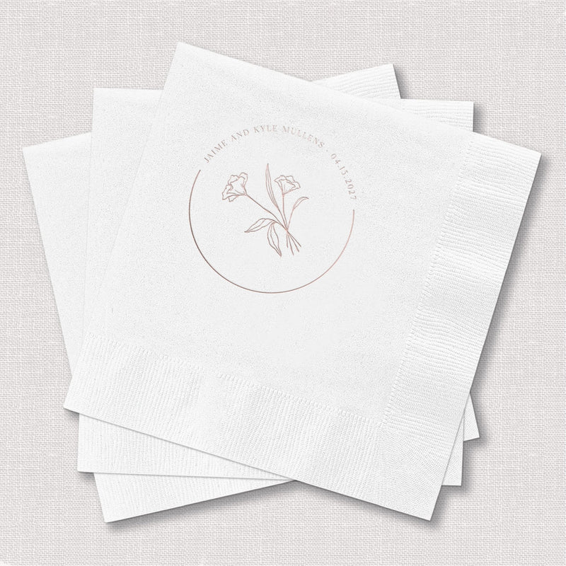 White cocktail napkins with delicate floral design and circular monogram in rose gold foil stamp