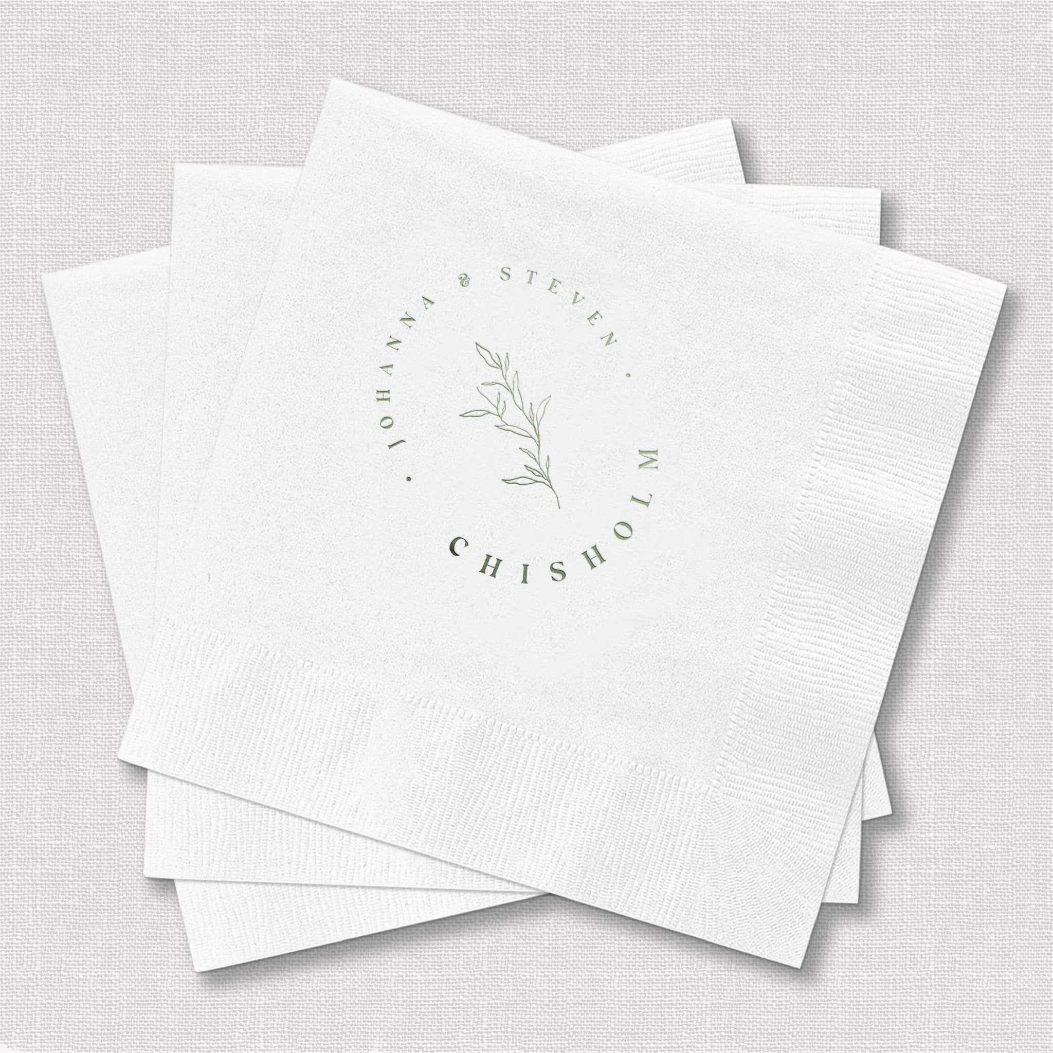 White foil-stamped napkins with delicate botanical design and circular text reading "here's to love laughter and happily ever after"