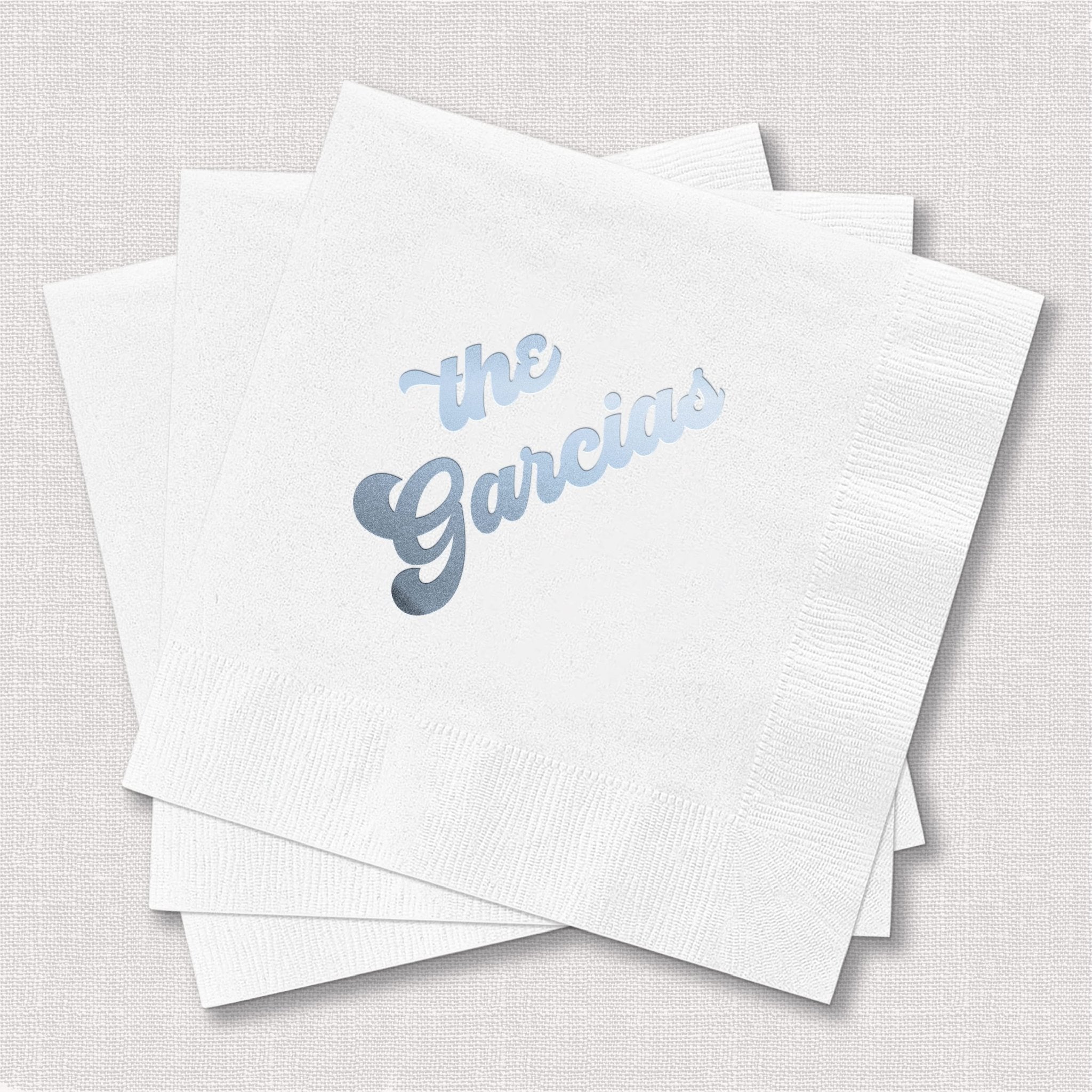Stack of white cocktail napkins with "the Garcias" printed in blue foil lettering