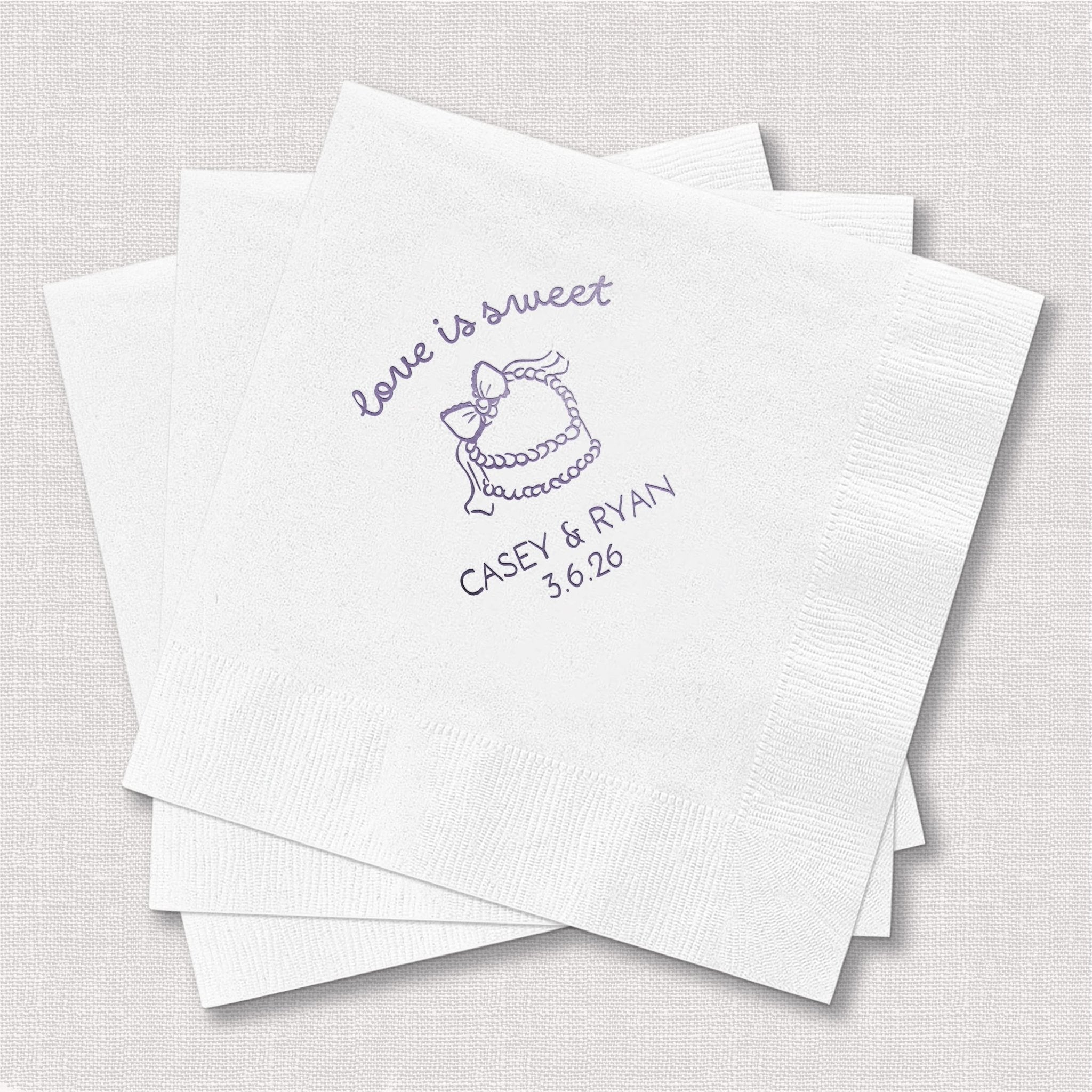 White cocktail napkins with purple foil-stamped design reading "love is sweet" and cupcake illustration, personalized with names and wedding date below.